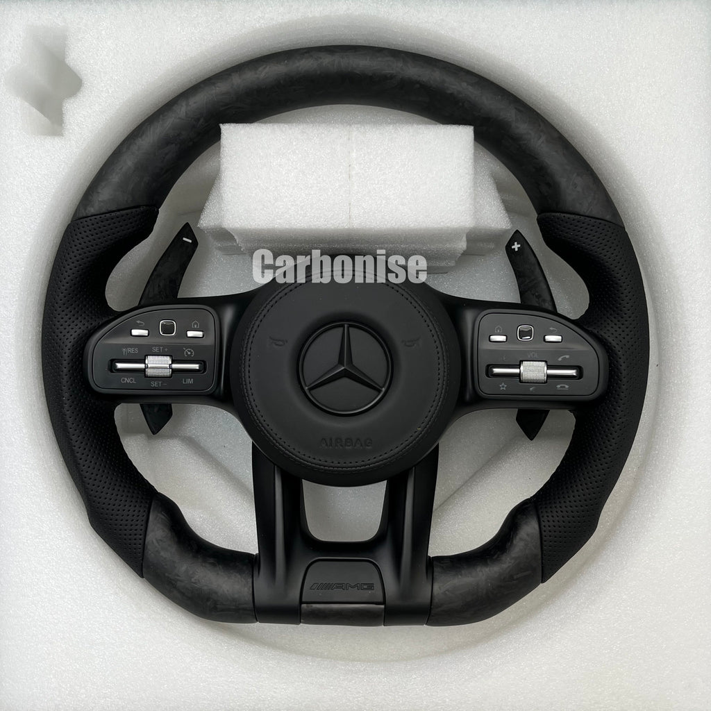 Custom Mercedes-Benz AMG steering wheel featuring forged carbon fiber with a marbled finish, black perforated leather grips, and all-black performance controls.