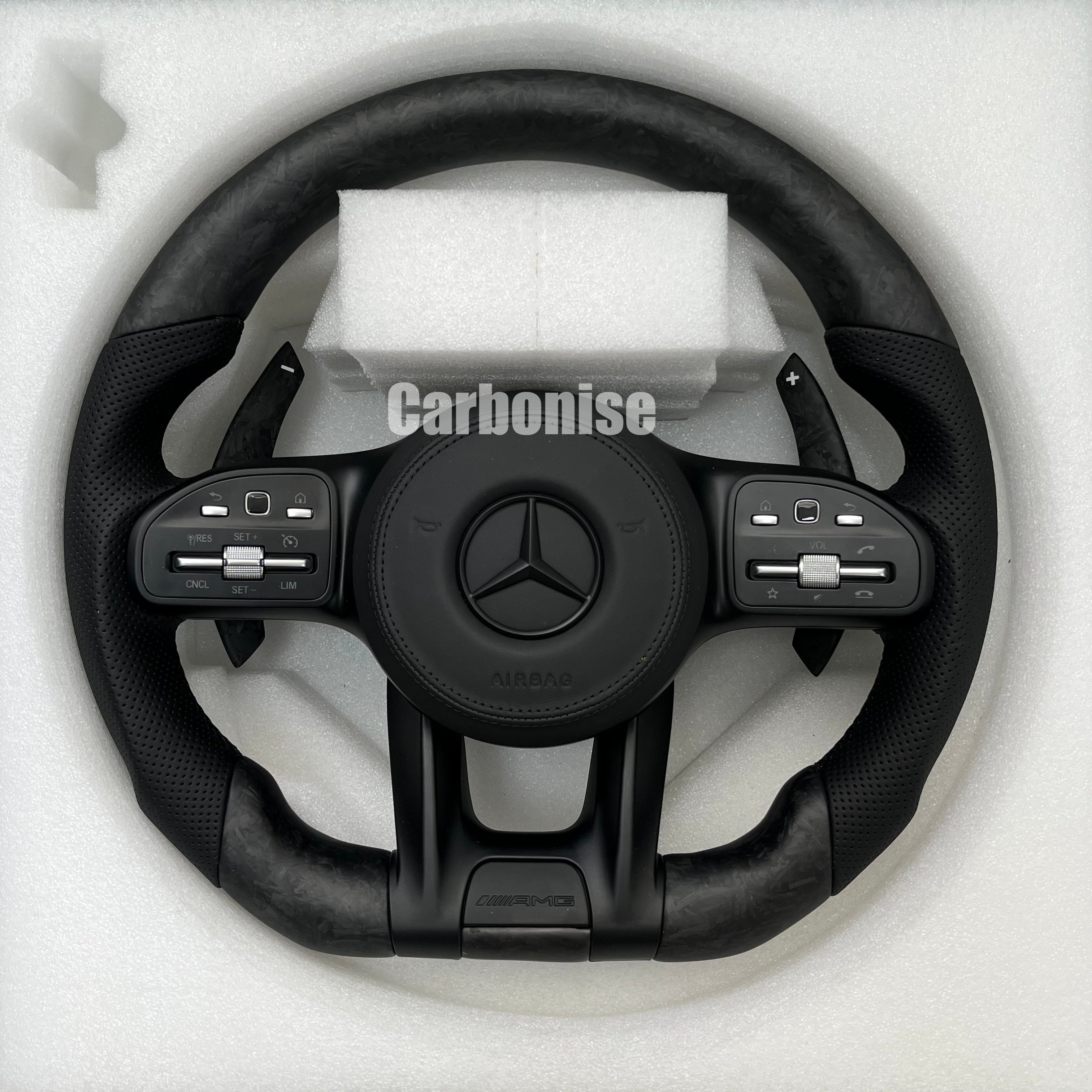 Custom Mercedes-Benz AMG steering wheel featuring forged carbon fiber with a marbled finish, black perforated leather grips, and all-black performance controls.