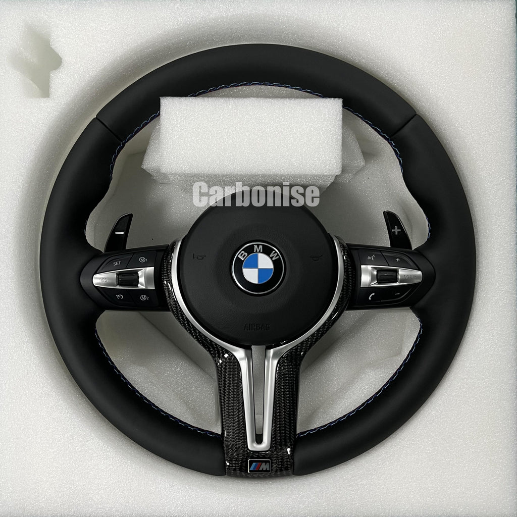 BMW M Performance steering wheel featuring a full black smooth leather wrap, blue contrast stitching, and a high-gloss carbon fiber bottom spoke trim.