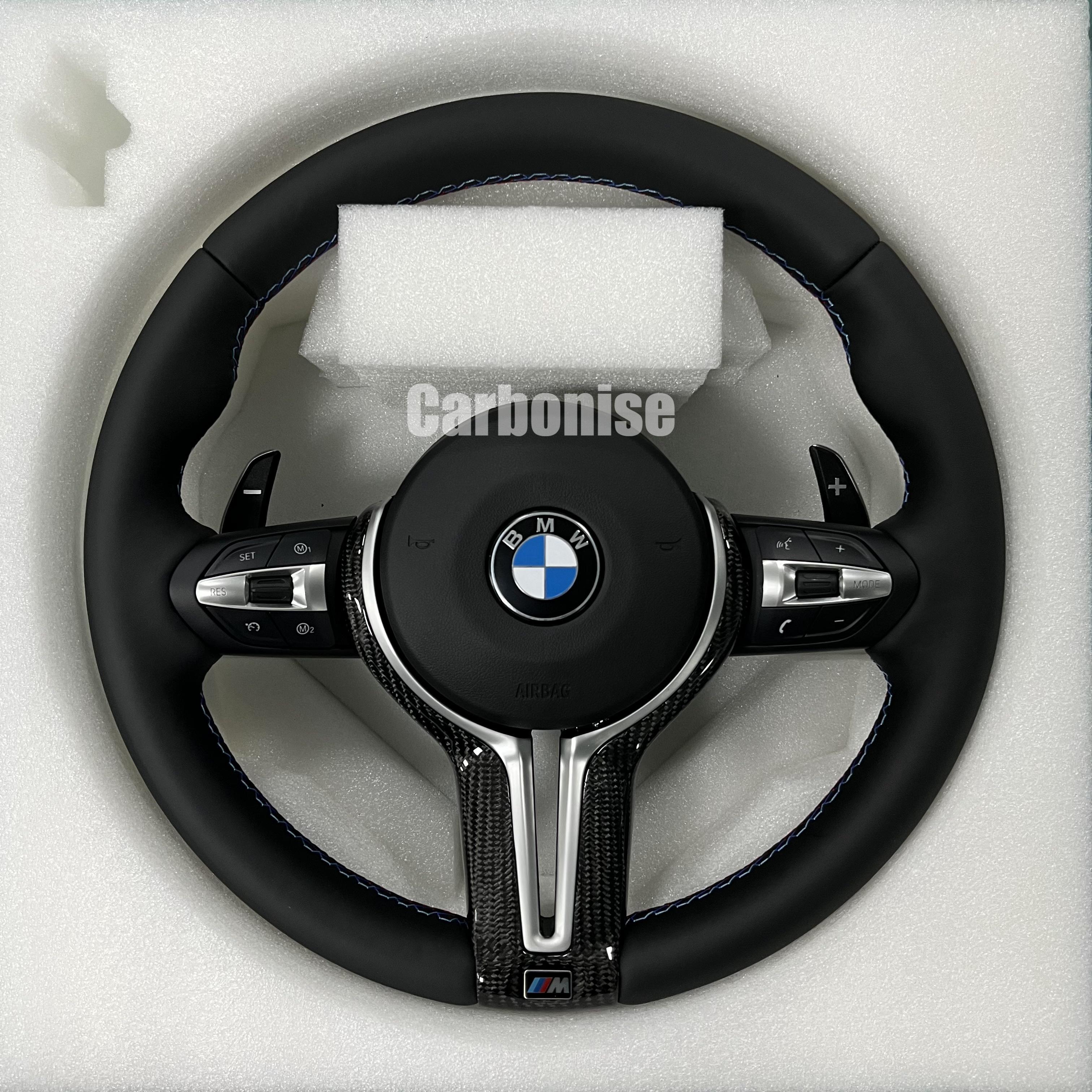 BMW M Performance steering wheel featuring a full black smooth leather wrap, blue contrast stitching, and a high-gloss carbon fiber bottom spoke trim.