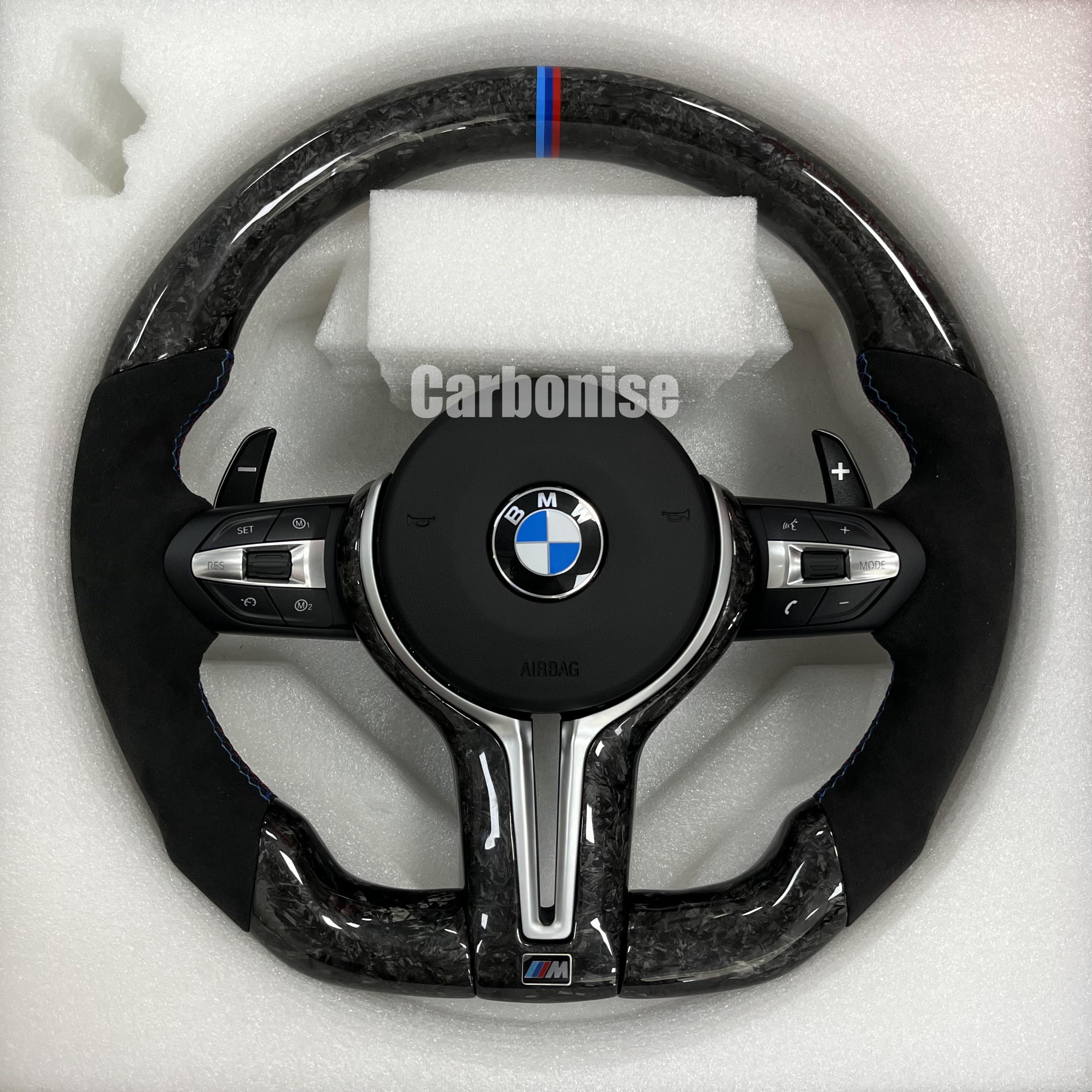 Custom BMW M performance steering wheel featuring a forged carbon fiber finish, black Alcantara side grips, and a signature M-tri color top racing stripe.