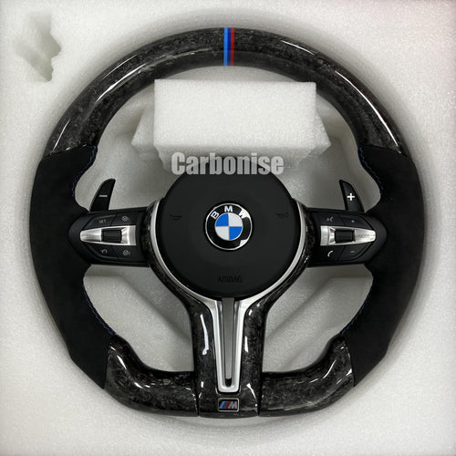 Custom BMW M performance steering wheel featuring a forged carbon fiber finish, black Alcantara side grips, and a signature M-tri color top racing stripe.