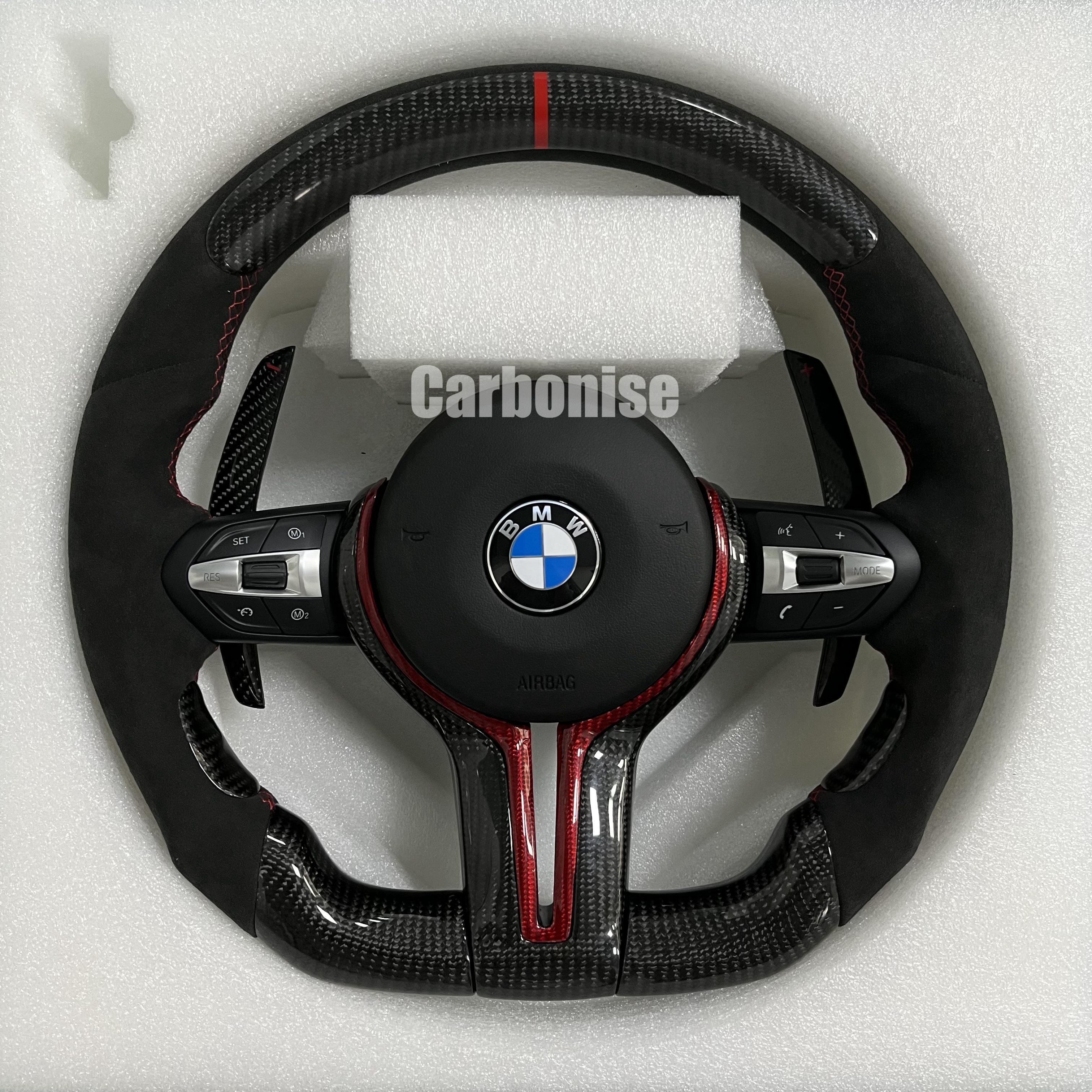 Custom BMW M performance steering wheel featuring gloss carbon fiber with red tinted accents, black Alcantara side grips, and a red racing stripe.