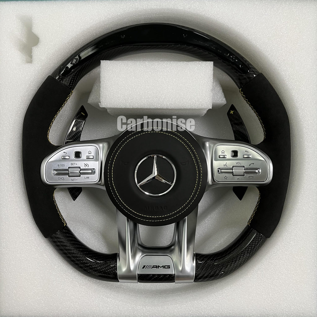 Custom Mercedes-Benz AMG steering wheel featuring a gloss carbon fiber top and bottom, black Alcantara side grips with yellow stitching, and silver controls.