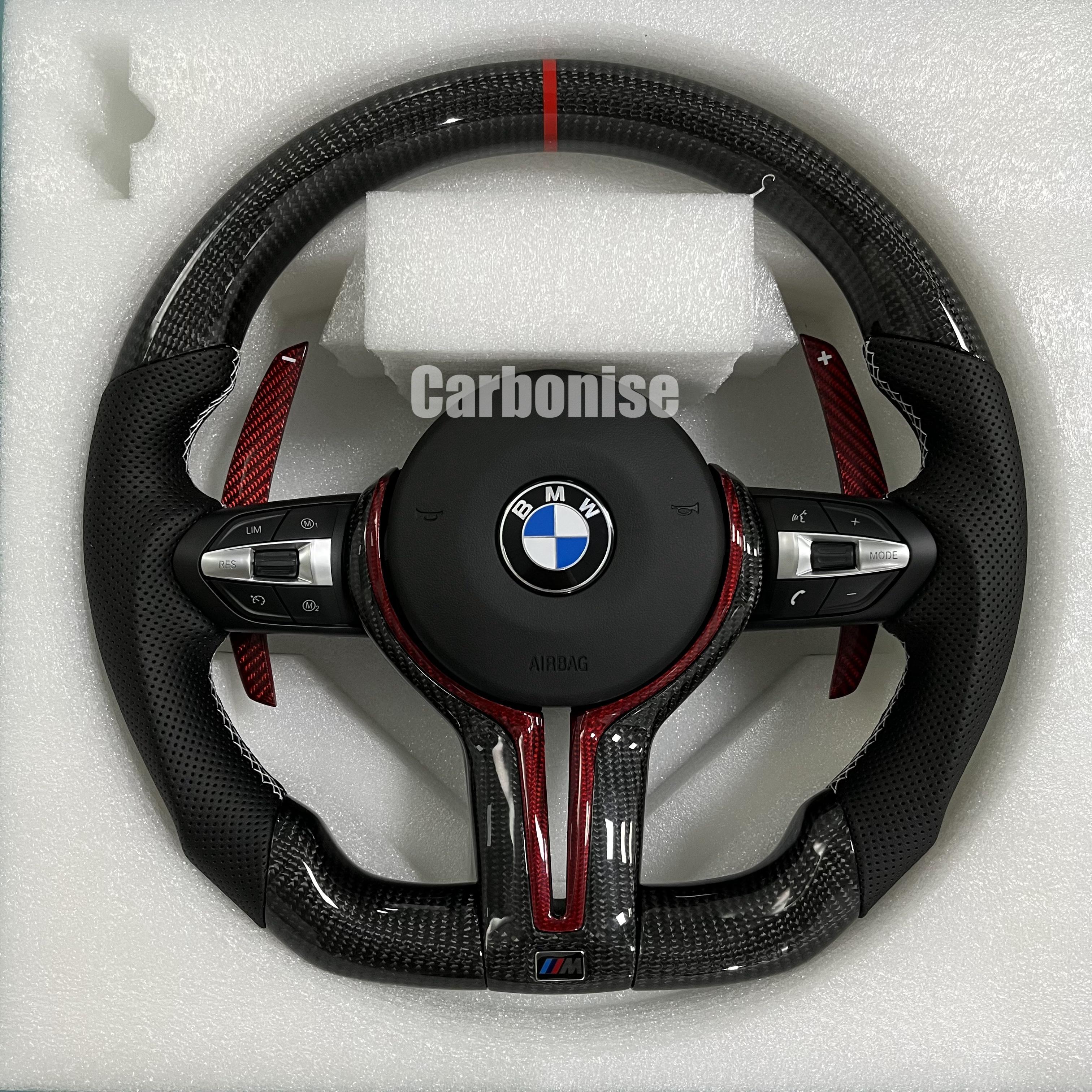 Custom BMW M steering wheel featuring gloss carbon fiber, a red top racing stripe, red tinted carbon accents, and perforated leather side grips.