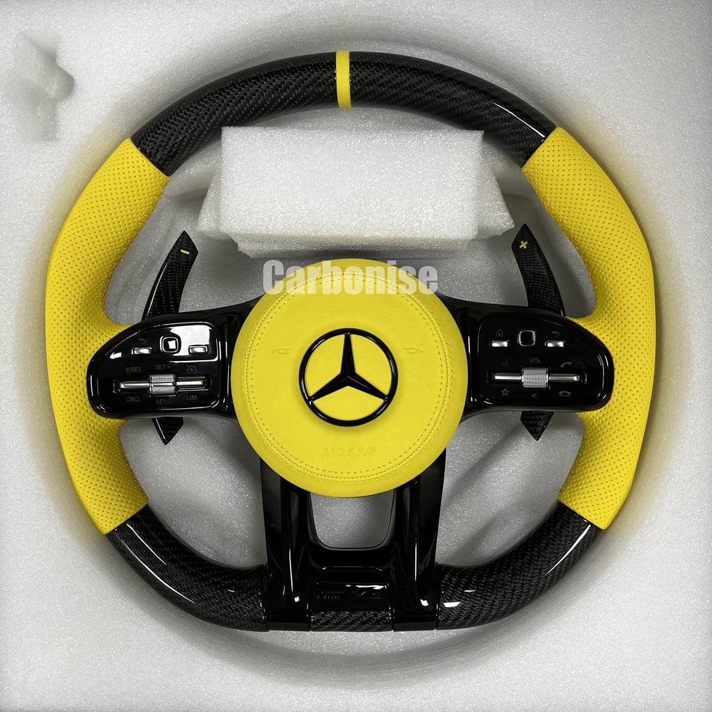 Custom Mercedes-Benz AMG steering wheel featuring high-gloss carbon fiber, a yellow leather airbag cover, and matching yellow perforated leather side grips.