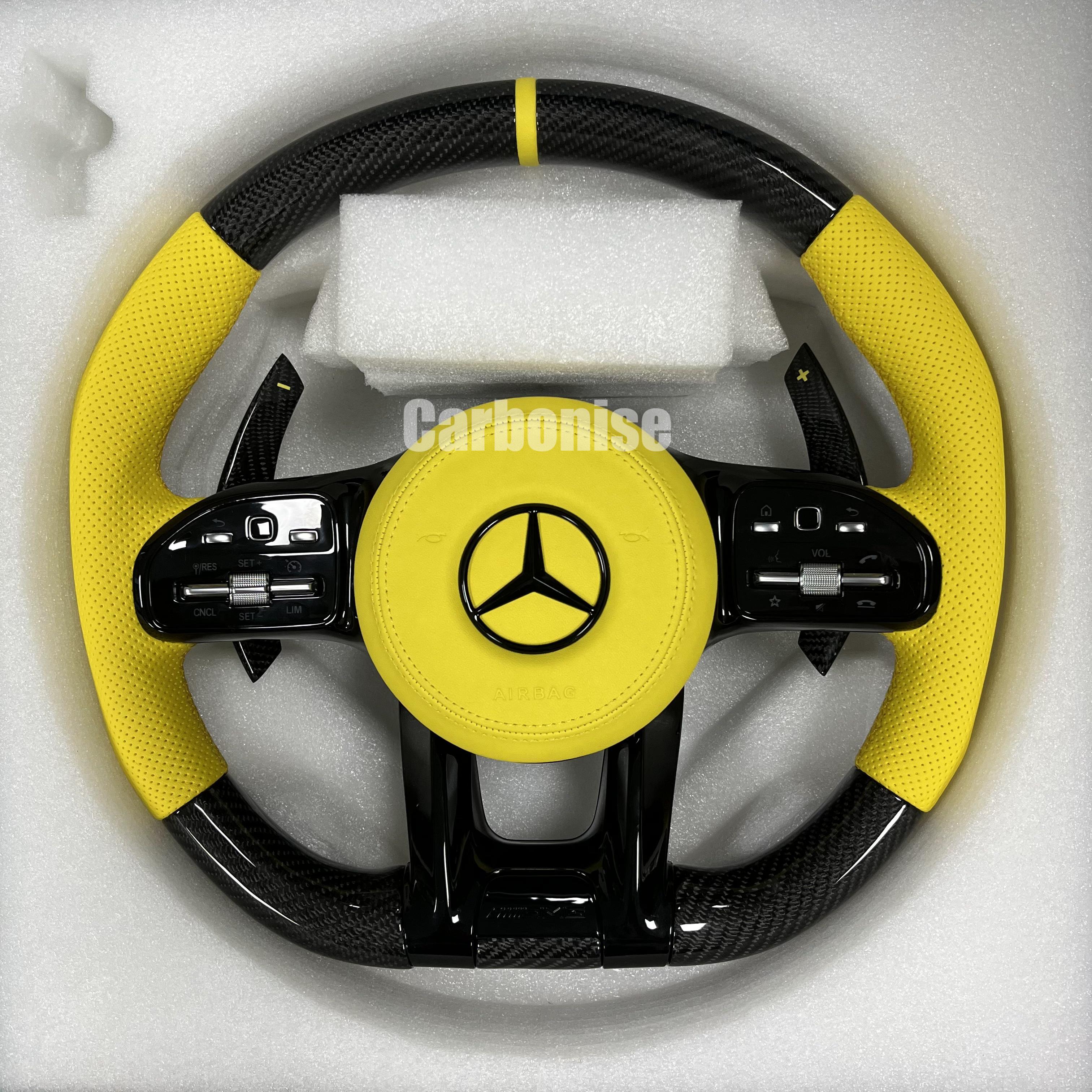 Custom Mercedes-Benz AMG steering wheel featuring high-gloss carbon fiber, a yellow leather airbag cover, and matching yellow perforated leather side grips.
