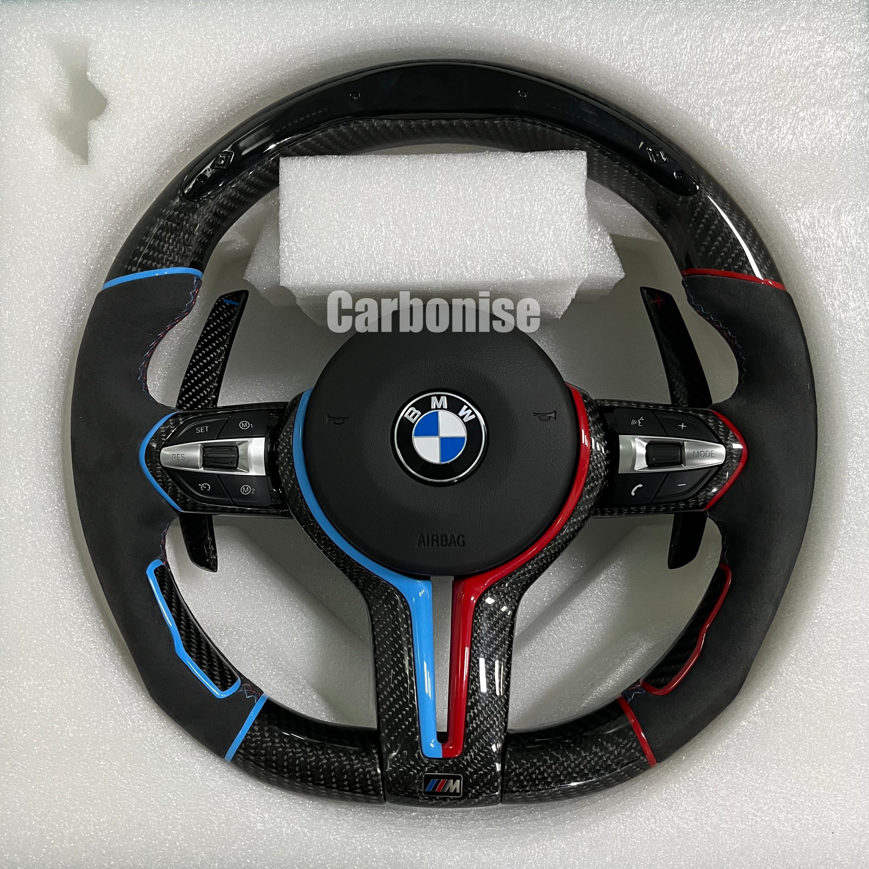 Custom BMW M performance steering wheel featuring gloss carbon fiber, black Alcantara side grips, and vibrant blue and red color-tinted accents.