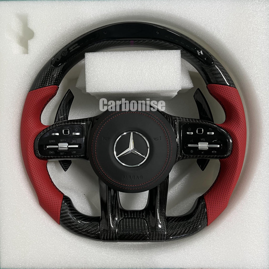 Custom Mercedes-Benz AMG performance steering wheel featuring gloss carbon fiber, a digital LED shift display, and vibrant red perforated leather side grips.
