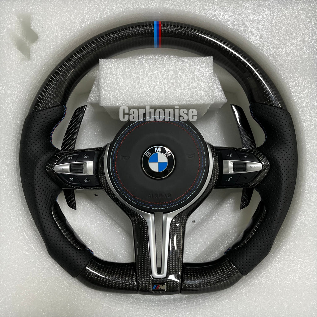 Custom BMW M performance steering wheel featuring high-gloss carbon fiber, a signature M-tri color top racing stripe, and black perforated leather grips.