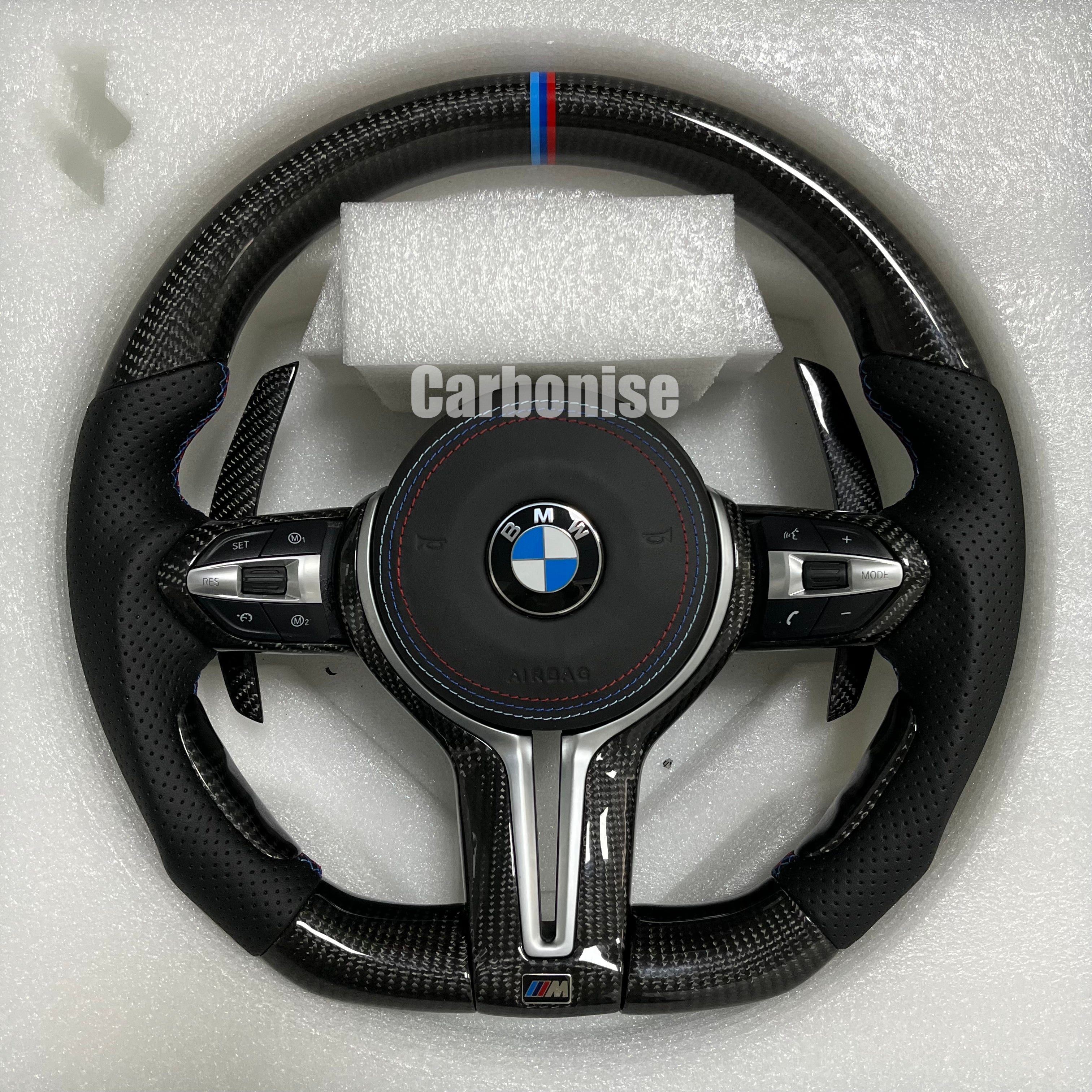 Custom BMW M performance steering wheel featuring high-gloss carbon fiber, a signature M-tri color top racing stripe, and black perforated leather grips.