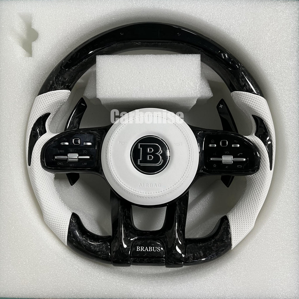 Custom Brabus performance steering wheel featuring high-gloss forged carbon fiber, arctic white perforated leather side grips, and a Brabus center logo.