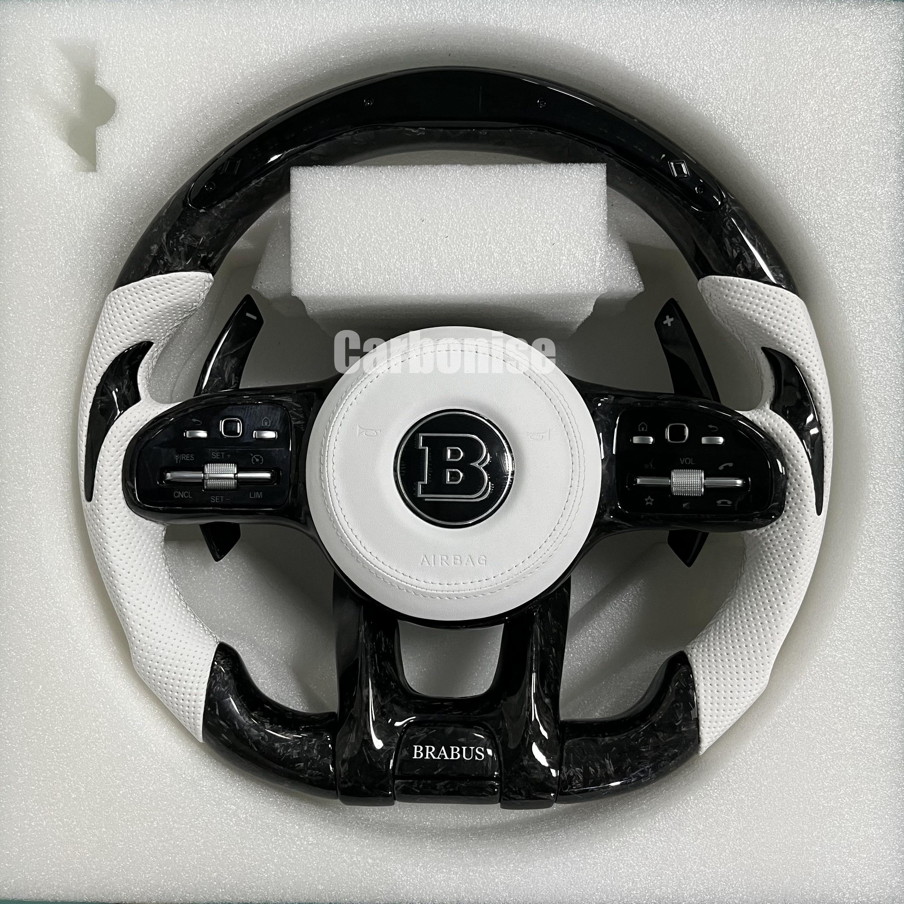 Custom Brabus performance steering wheel featuring high-gloss forged carbon fiber, arctic white perforated leather side grips, and a Brabus center logo.