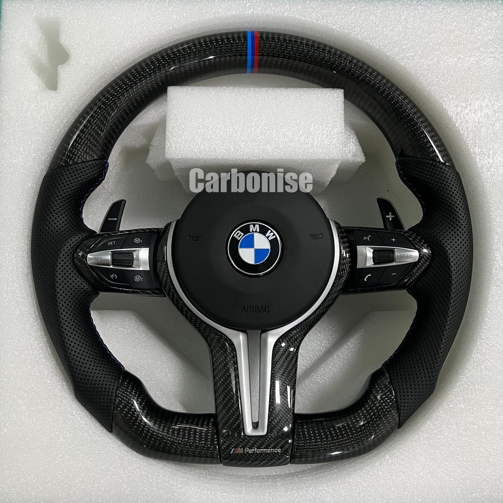 BMW M Performance steering wheel featuring gloss carbon fiber, a signature blue, light blue, and red M-tri color top racing stripe, and black perforated leather side grips with blue stitching.