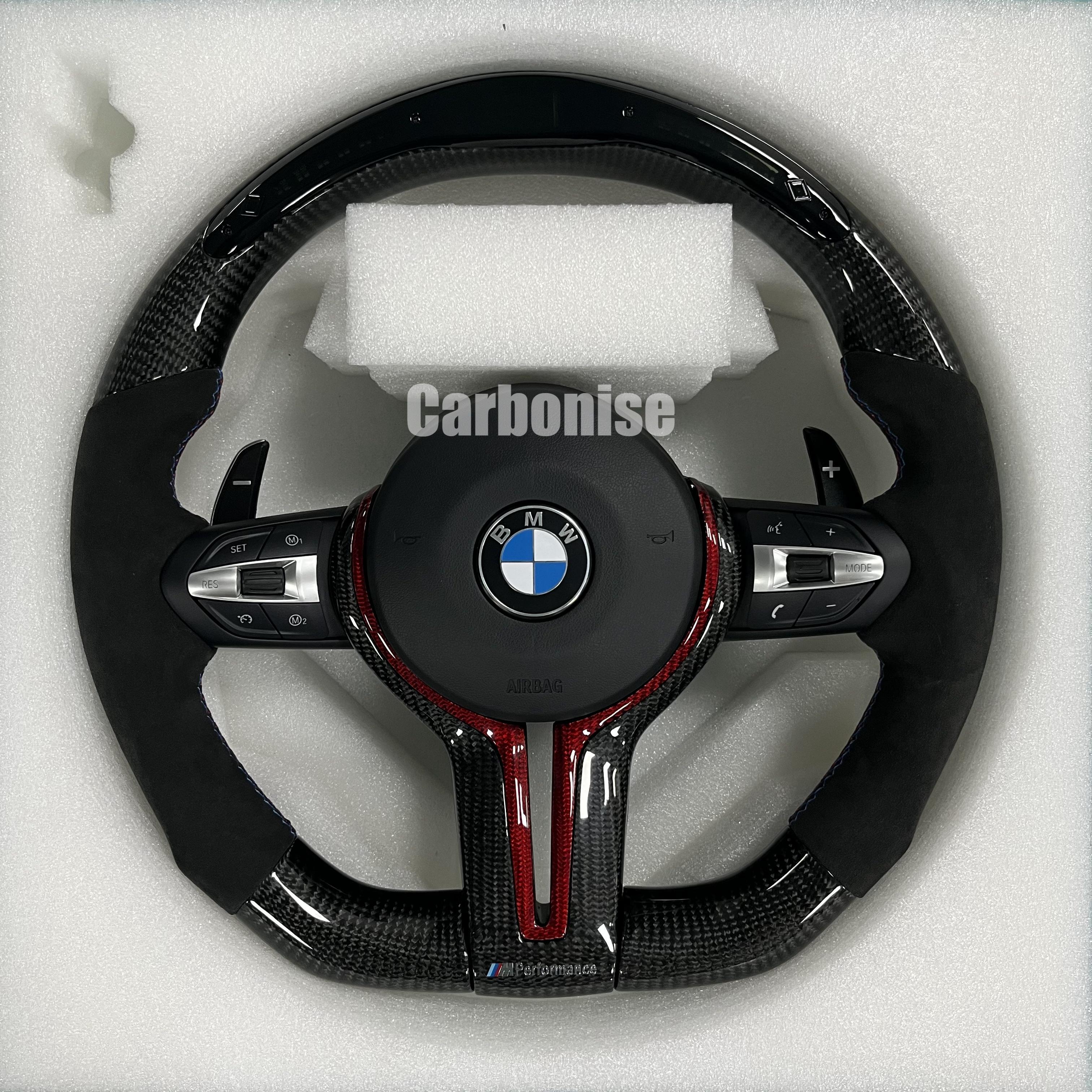 Custom BMW M performance steering wheel featuring gloss carbon fiber with red tinted accents, black Alcantara side grips, and red stitching.