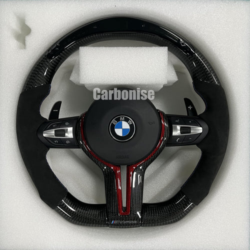 Custom BMW M performance steering wheel featuring gloss carbon fiber with red tinted accents, black Alcantara side grips, and red stitching.