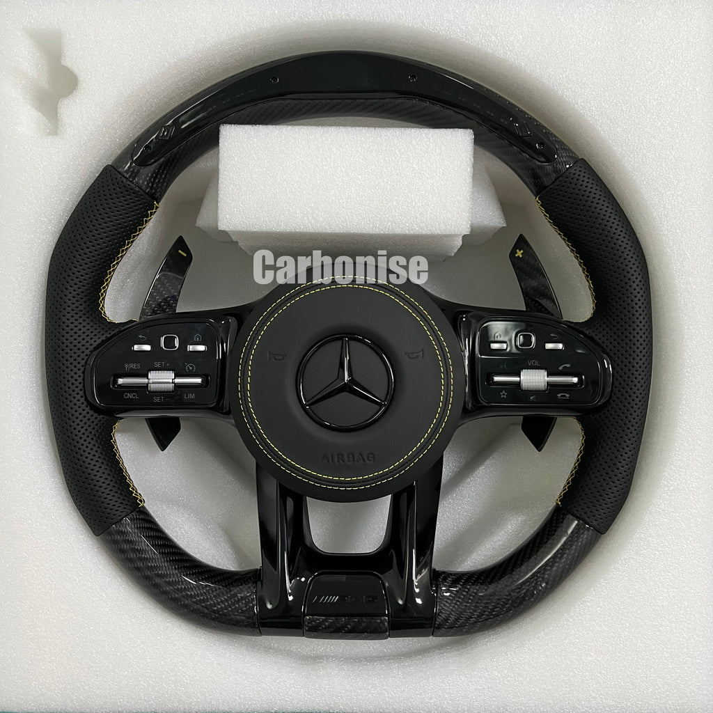 Custom Mercedes-Benz AMG steering wheel featuring high-gloss carbon fiber, black perforated leather side grips with yellow stitching, and yellow performance accents.