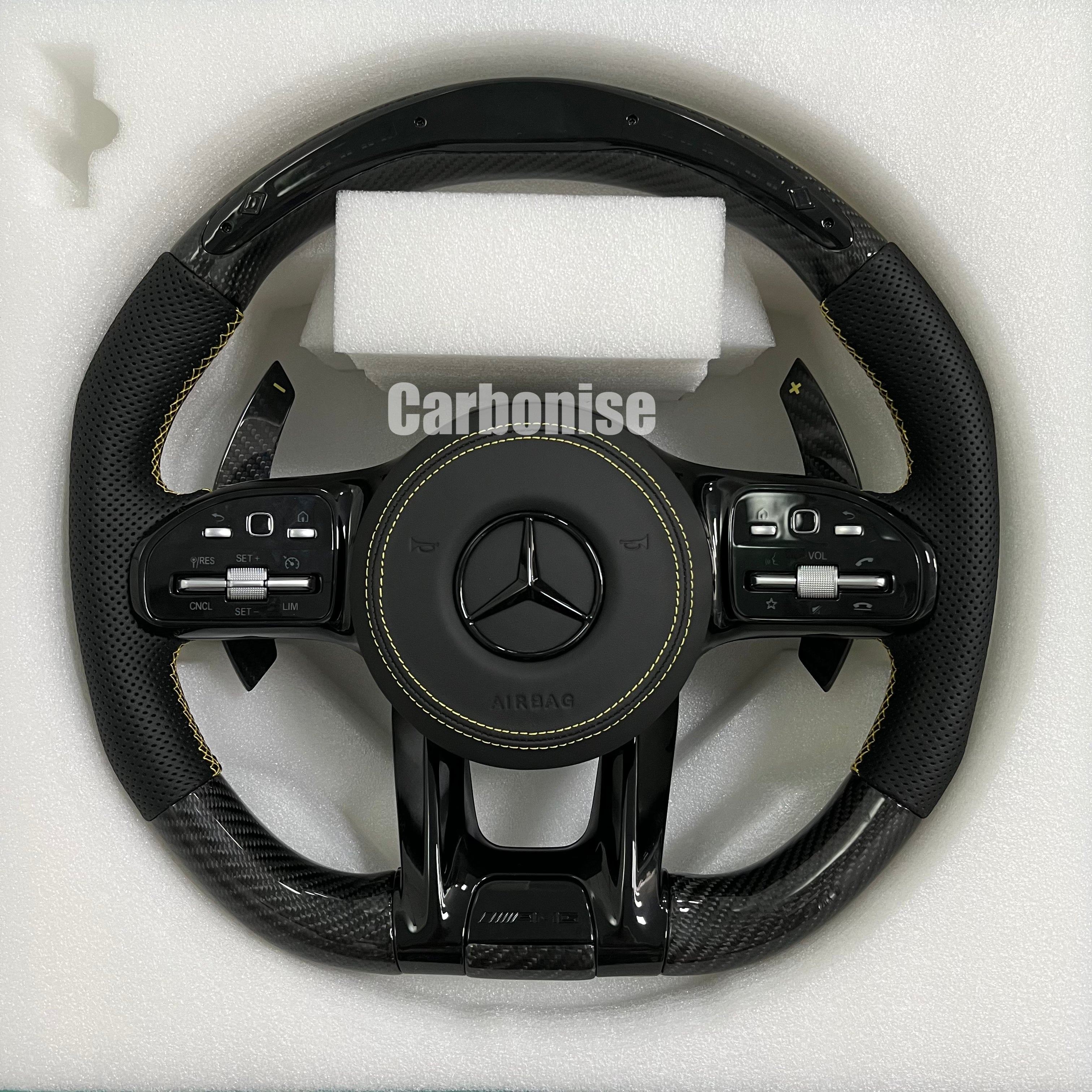 Custom Mercedes-Benz AMG steering wheel featuring high-gloss carbon fiber, black perforated leather side grips with yellow stitching, and yellow performance accents.