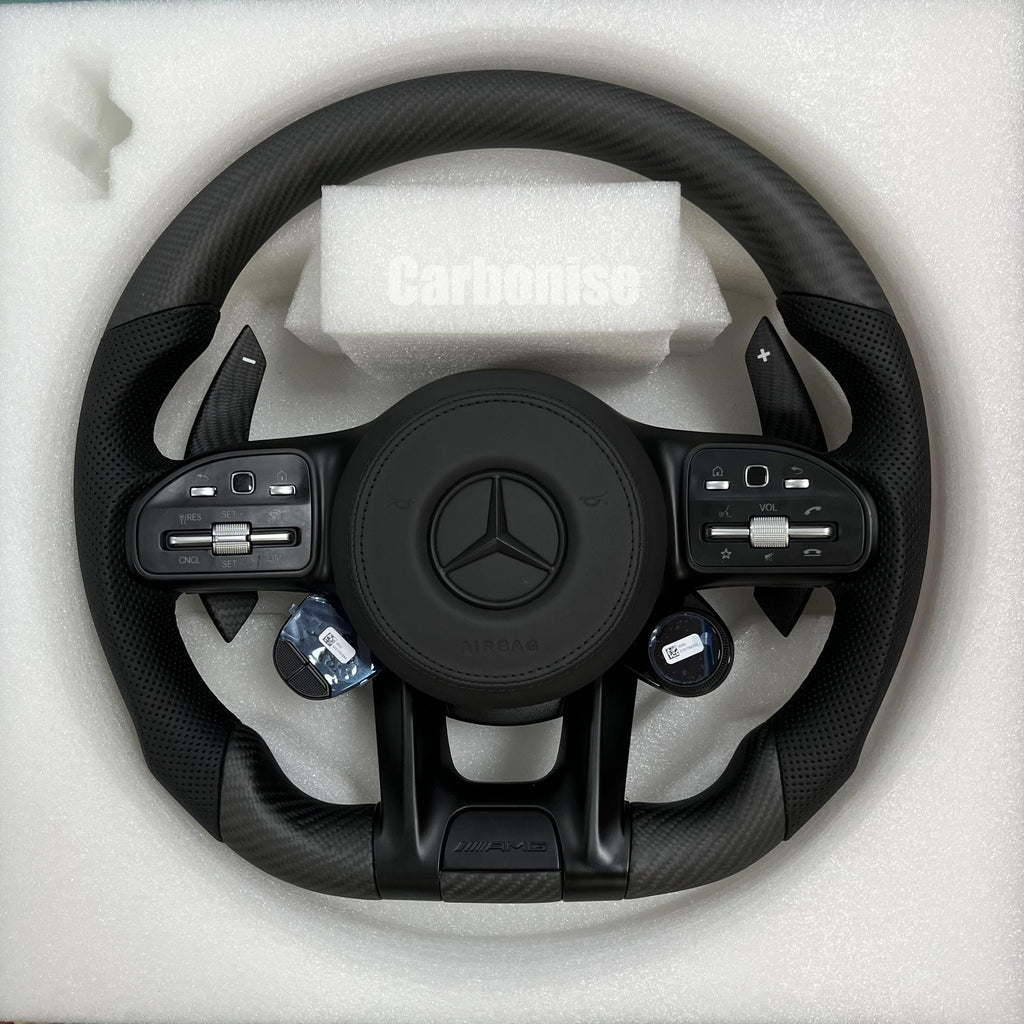 Custom Mercedes-Benz AMG steering wheel featuring matte carbon fiber, integrated digital drive mode dials, and black perforated leather side grips.