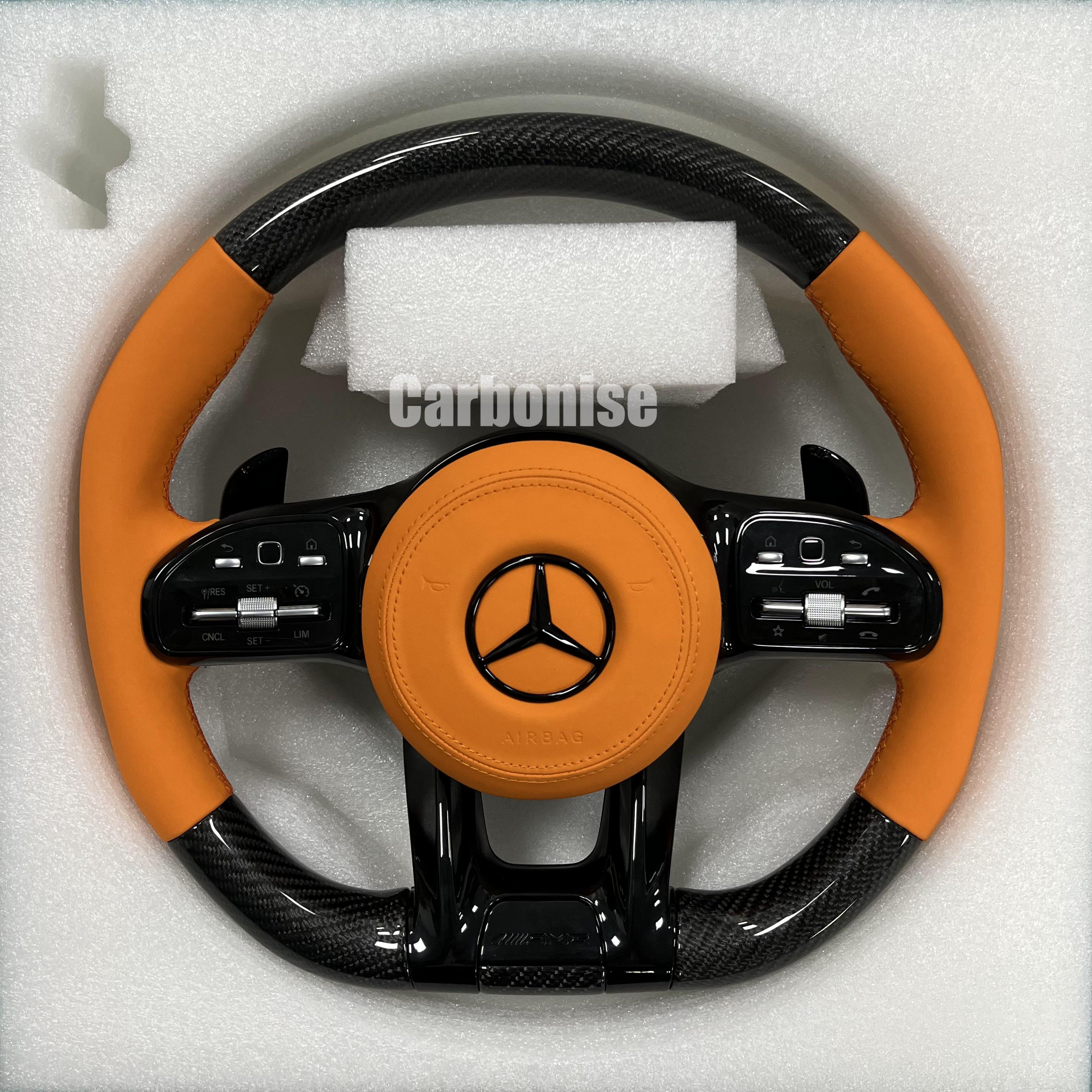 Custom Mercedes-Benz AMG steering wheel featuring high-gloss carbon fiber, a vibrant orange leather airbag cover, and matching orange leather side grips.