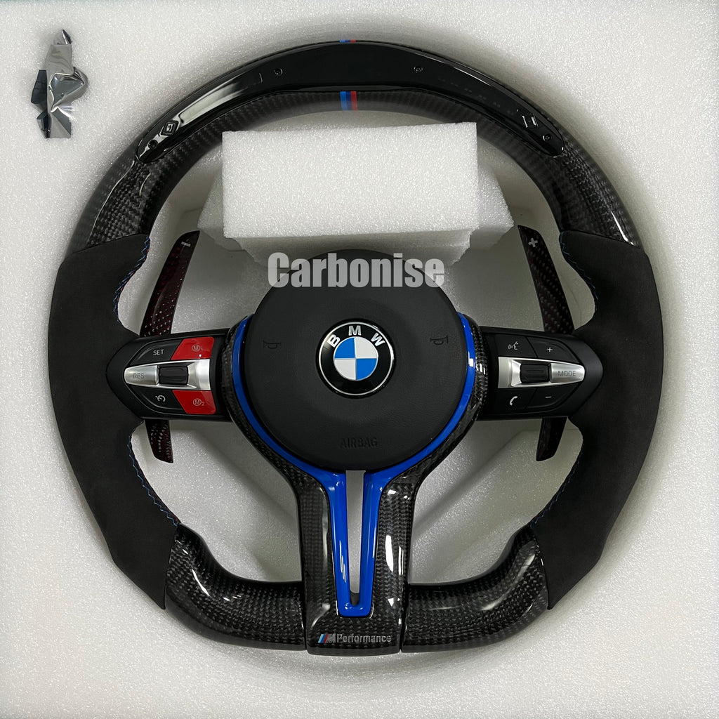 Custom BMW M steering wheel featuring gloss carbon fiber, black Alcantara grips, blue tinted carbon accents, and a signature M-tri color racing stripe.