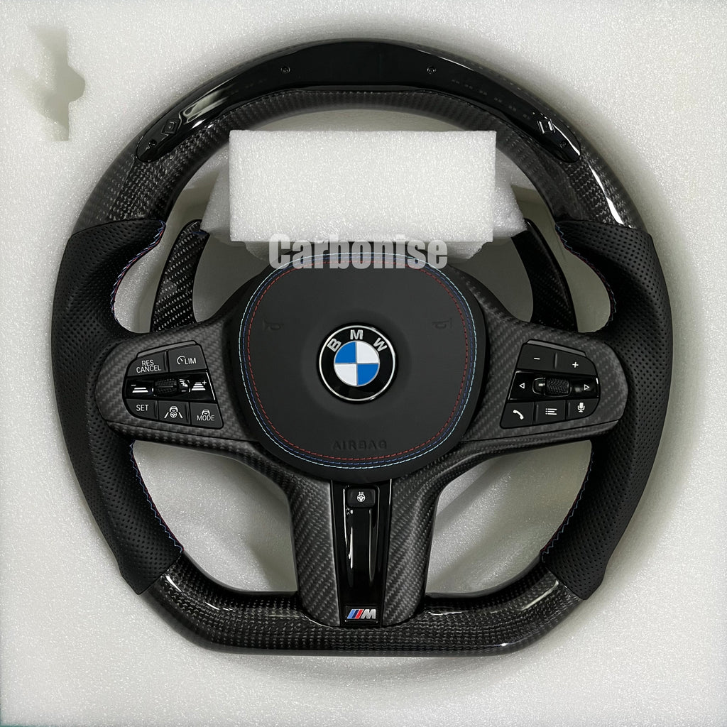 Custom BMW M performance steering wheel featuring high-gloss carbon fiber on the top and bottom with black perforated leather side grips and blue stitching.