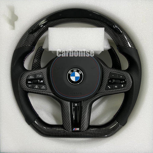 Custom BMW M performance steering wheel featuring high-gloss carbon fiber on the top and bottom with black perforated leather side grips and blue stitching.