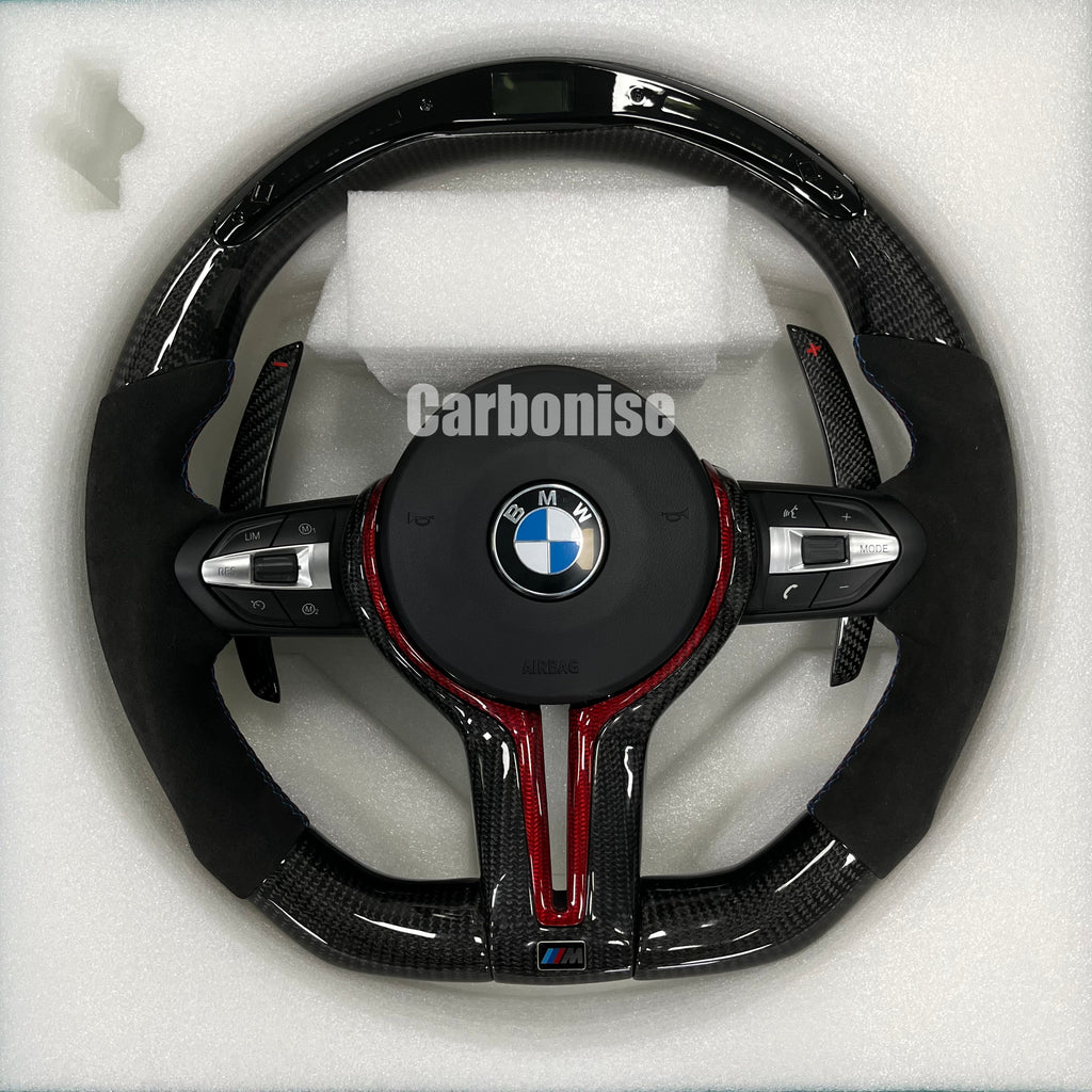Custom BMW M performance steering wheel featuring gloss carbon fiber with a digital LED display, red tinted accents, and black Alcantara side grips.