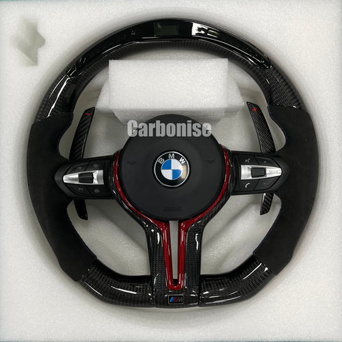 Custom BMW M performance steering wheel featuring gloss carbon fiber with a digital LED display, red tinted accents, and black Alcantara side grips.