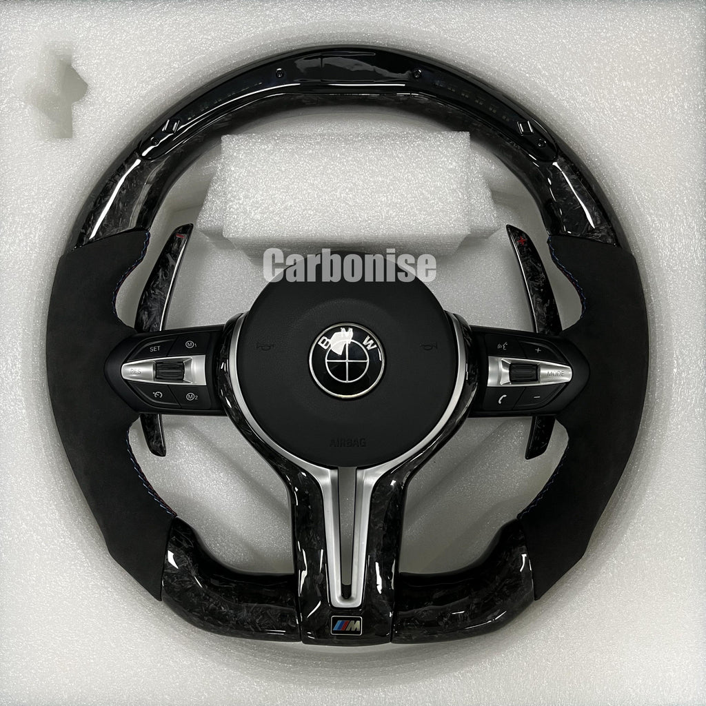 Custom BMW M performance steering wheel featuring a forged carbon fiber finish, black Alcantara side grips, and blue performance stitching.
