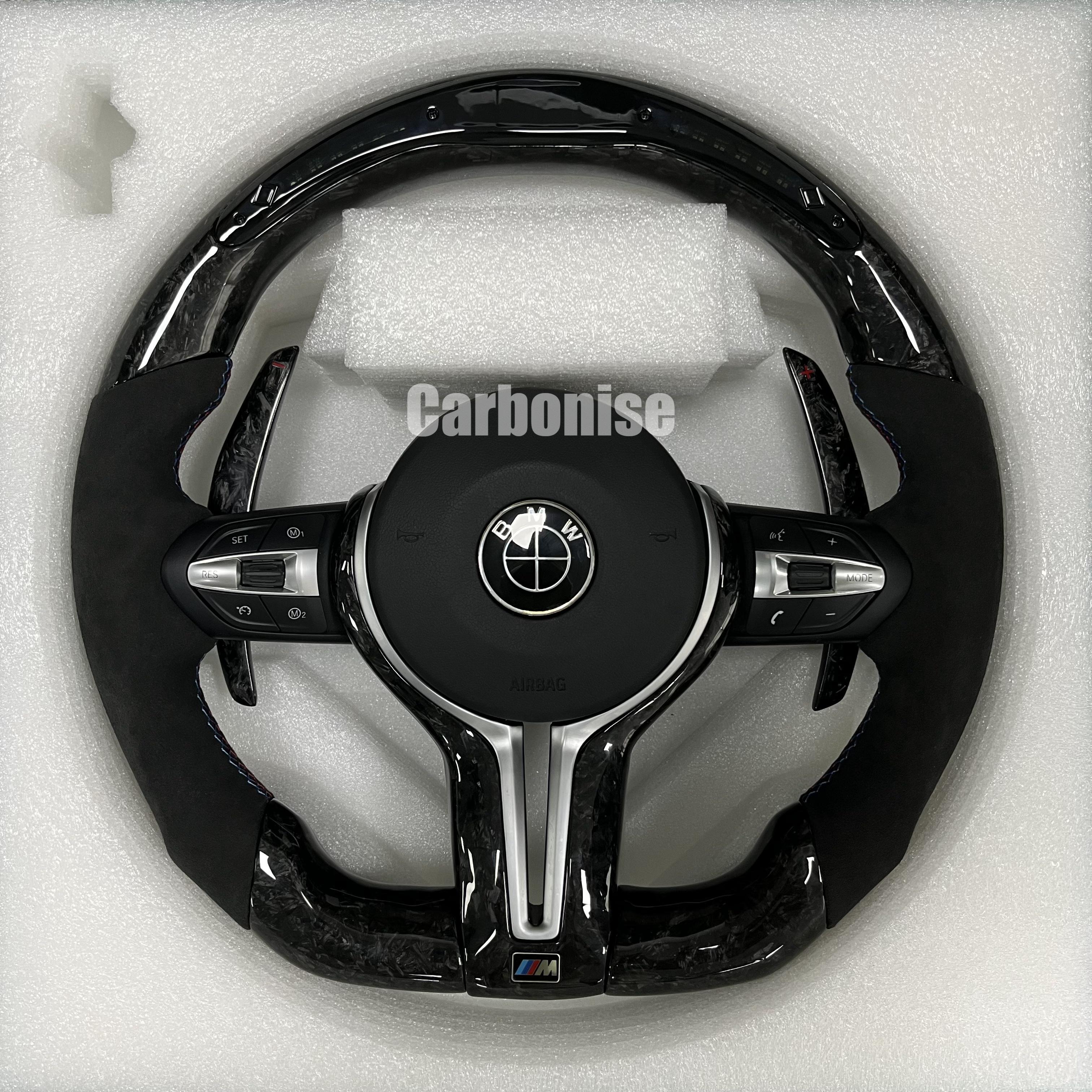 Custom BMW M performance steering wheel featuring a forged carbon fiber finish, black Alcantara side grips, and blue performance stitching.