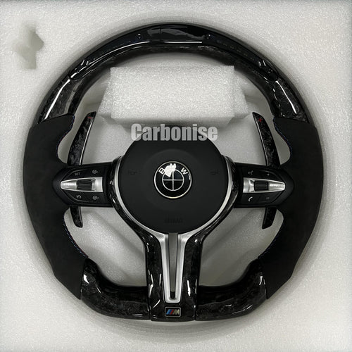 Custom BMW M performance steering wheel featuring a forged carbon fiber finish, black Alcantara side grips, and blue performance stitching.