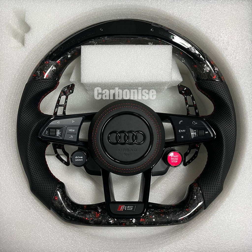 Custom Audi RS steering wheel in forged carbon fiber with red flakes, featuring black perforated leather grips, red stitching, and integrated red Start/Stop and black Drive Select buttons.