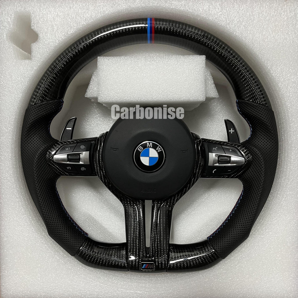 Custom BMW M Performance steering wheel featuring gloss carbon fiber, a signature blue, light blue, and red M-tri color top racing stripe, and black perforated leather side grips with blue stitching.