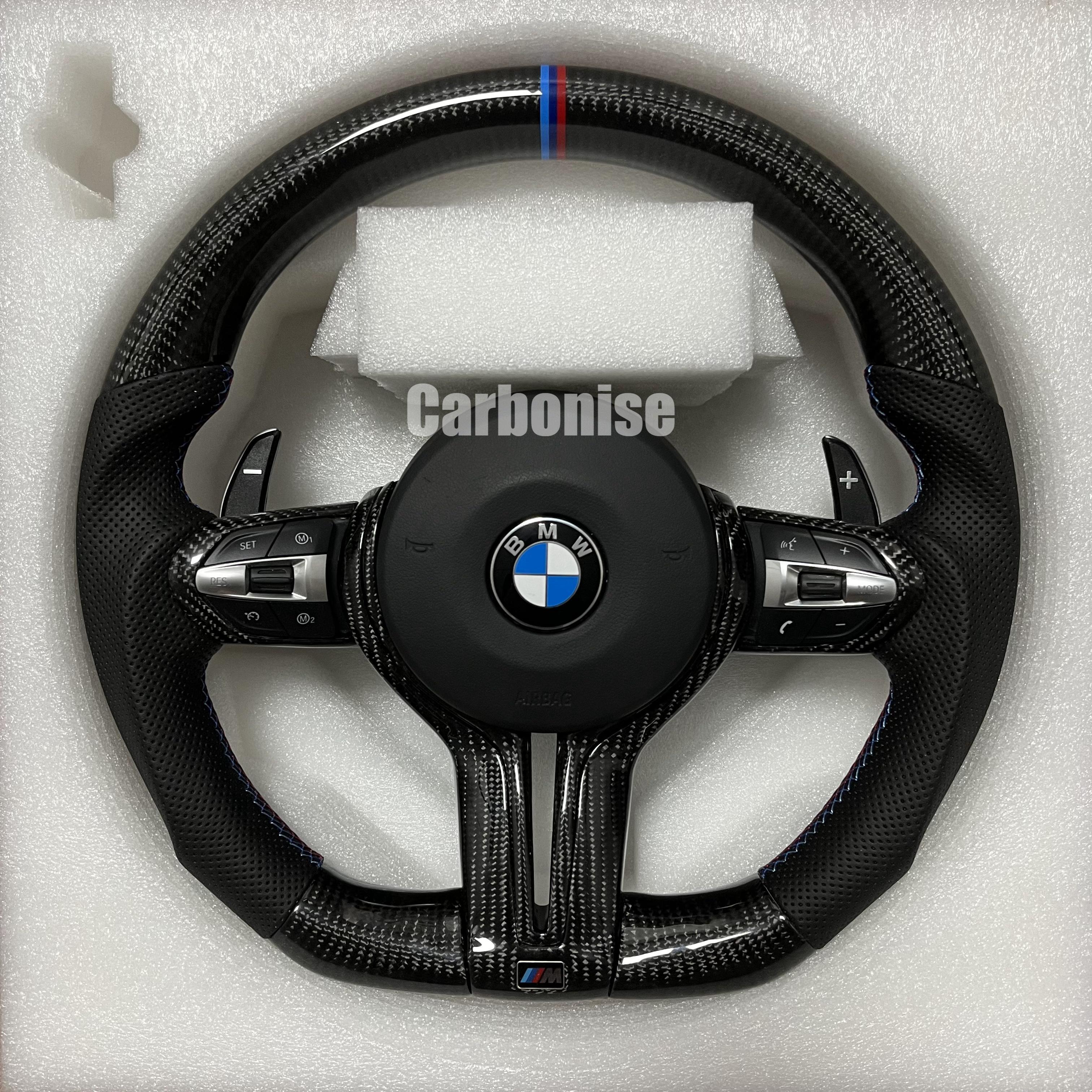 Custom BMW M Performance steering wheel featuring gloss carbon fiber, a signature blue, light blue, and red M-tri color top racing stripe, and black perforated leather side grips with blue stitching.