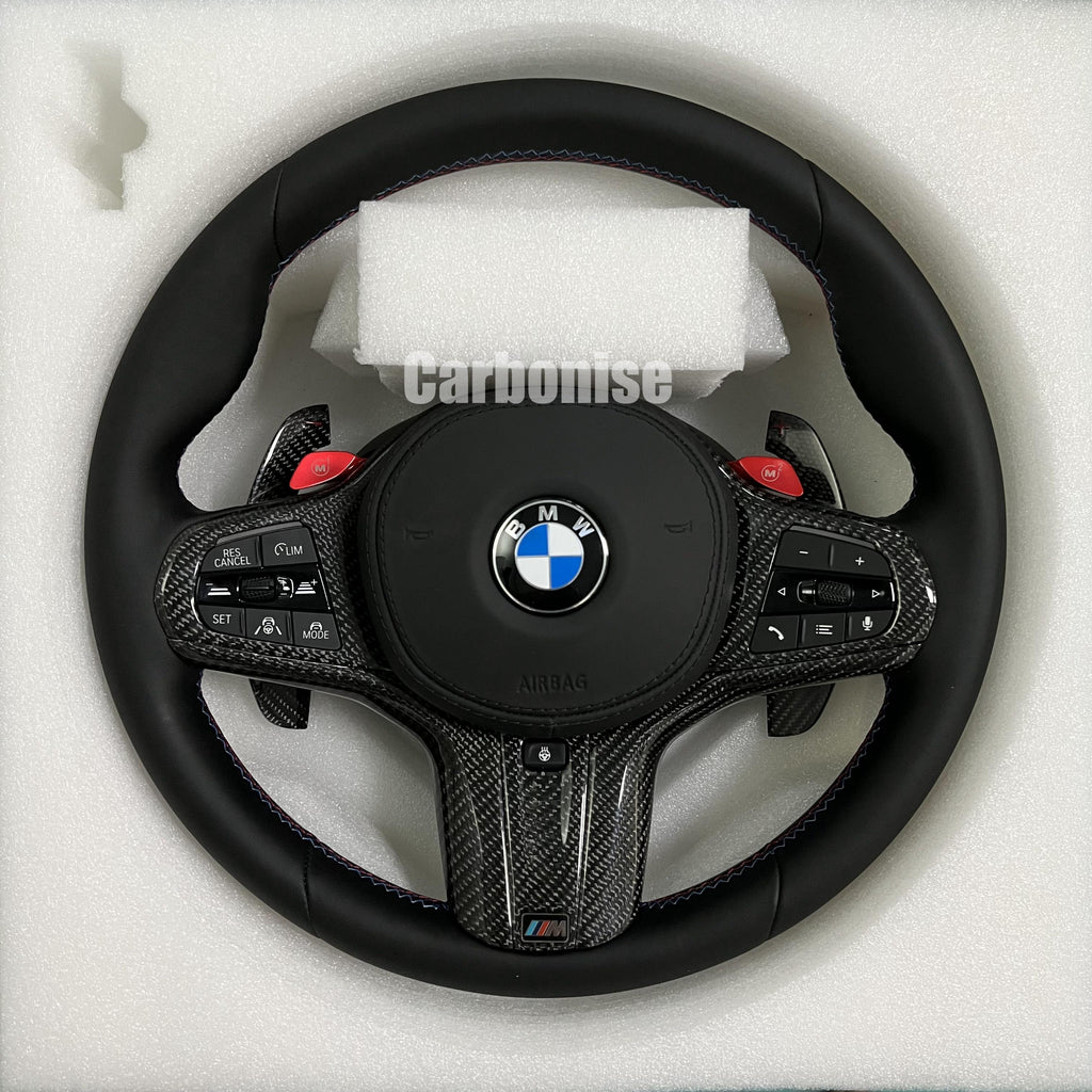 Custom BMW M performance steering wheel featuring a full black smooth leather wrap, red M1/M2 button accents, and high-gloss carbon fiber trim.