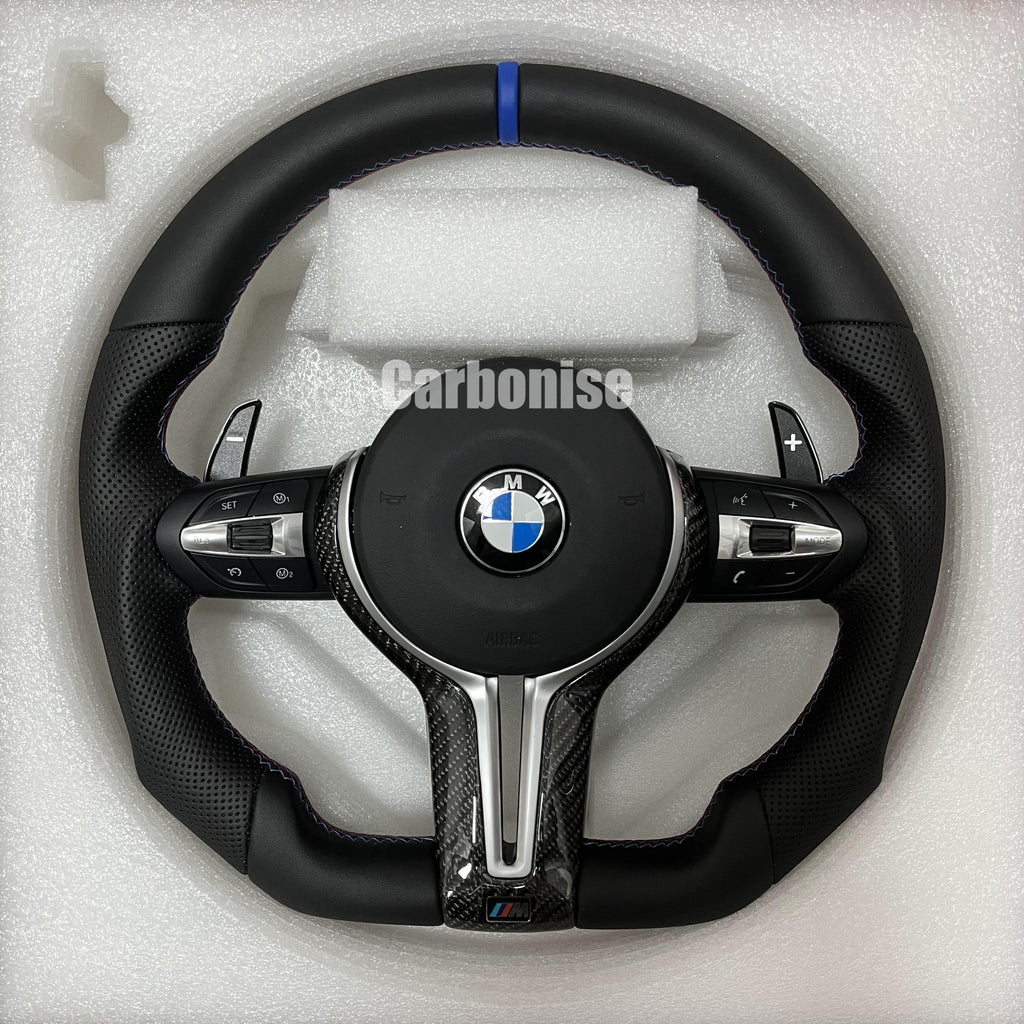 Custom BMW M Performance steering wheel featuring a blue top racing stripe, a mix of black smooth and perforated leather grips with blue stitching, and high-gloss carbon fiber trim.
