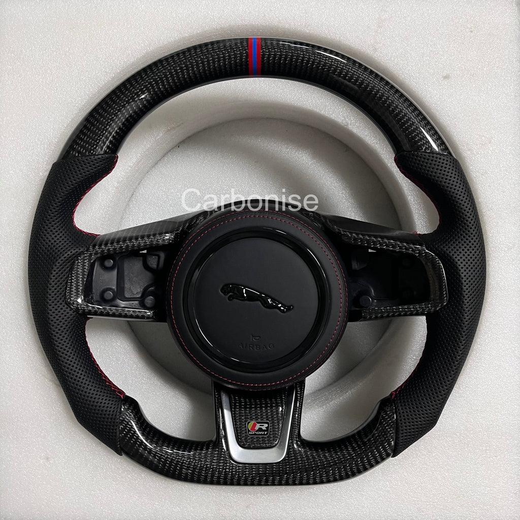 Custom Jaguar R carbon fibre steering wheel with perforated black leather grips, red stitching, tricolour top stripe, and flat-bottom performance design.