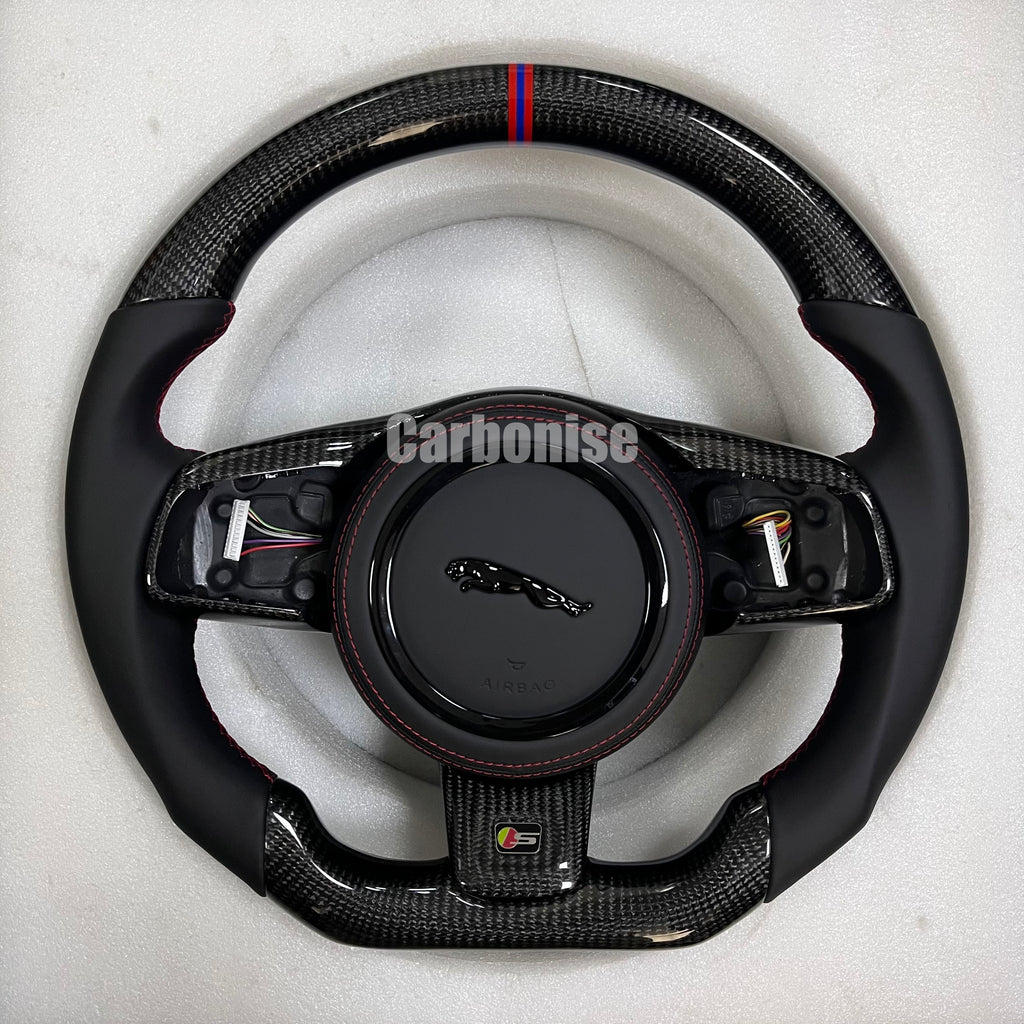 Custom Jaguar R carbon fibre steering wheel with smooth black leather grips, gloss carbon trim, red and blue centre alignment stripe, and flat-bottom performance design.