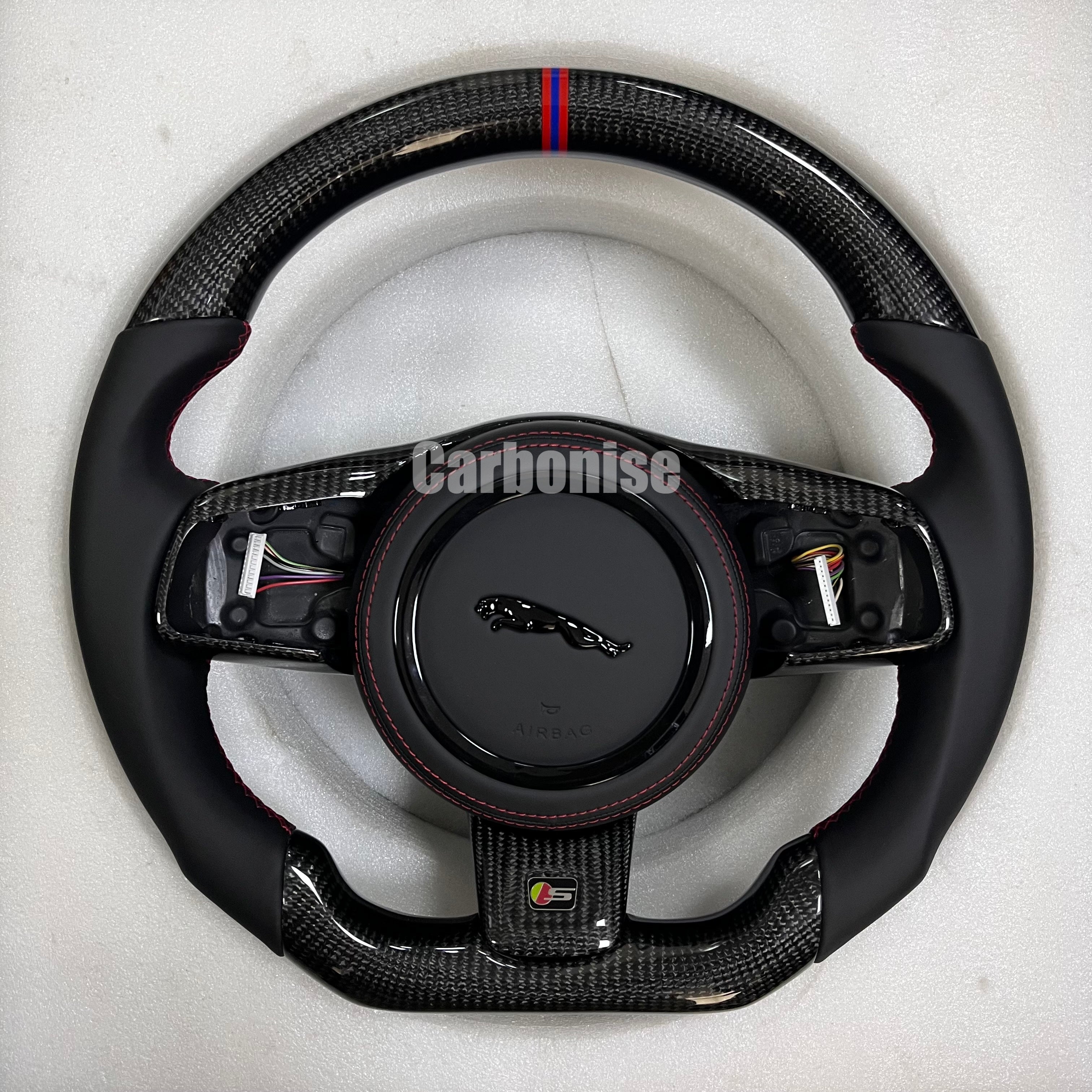 Custom Jaguar R carbon fibre steering wheel with smooth black leather grips, gloss carbon trim, red and blue centre alignment stripe, and flat-bottom performance design.