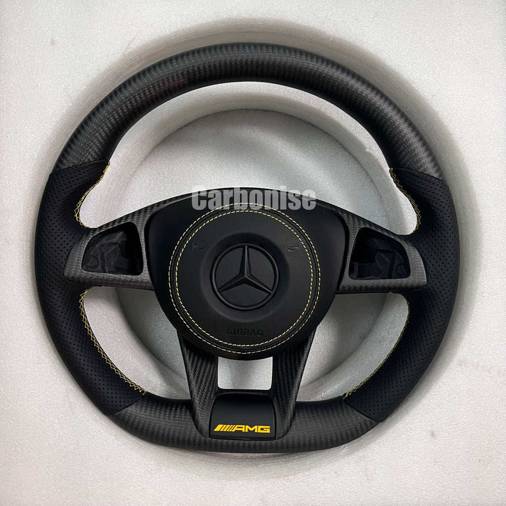 Custom Mercedes-Benz AMG steering wheel featuring a matte carbon fiber finish, black perforated leather grips with yellow stitching, and a yellow AMG lower logo.