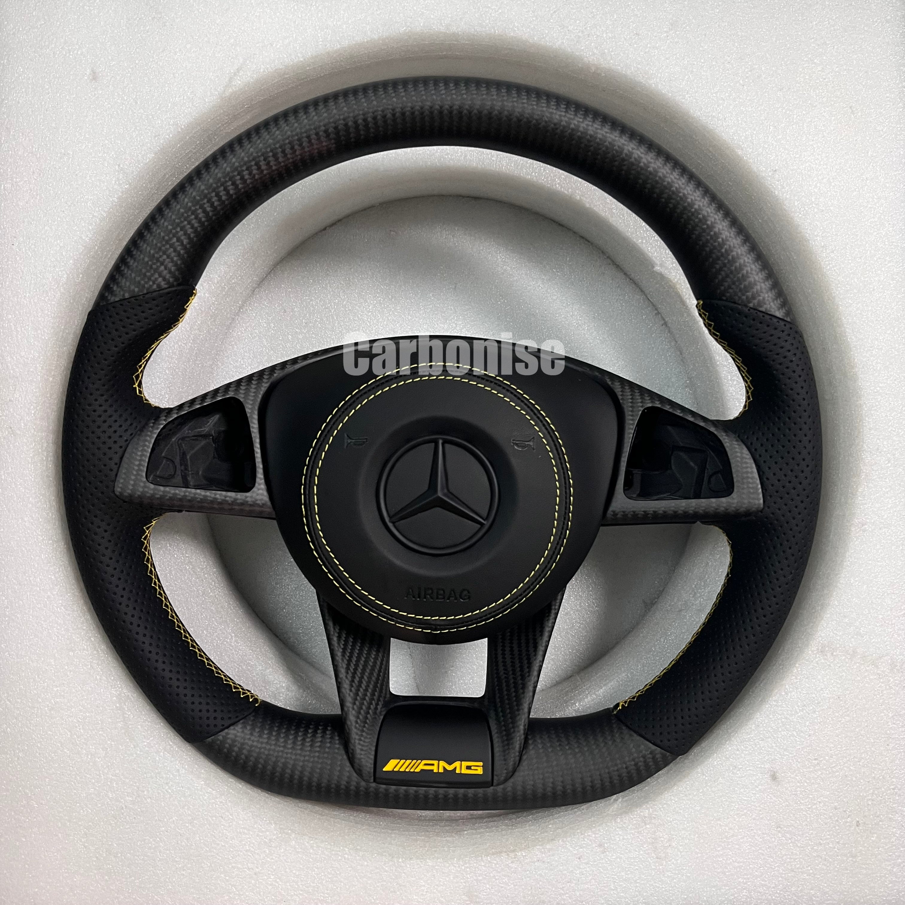 Custom Mercedes-Benz AMG steering wheel featuring a matte carbon fiber finish, black perforated leather grips with yellow stitching, and a yellow AMG lower logo.