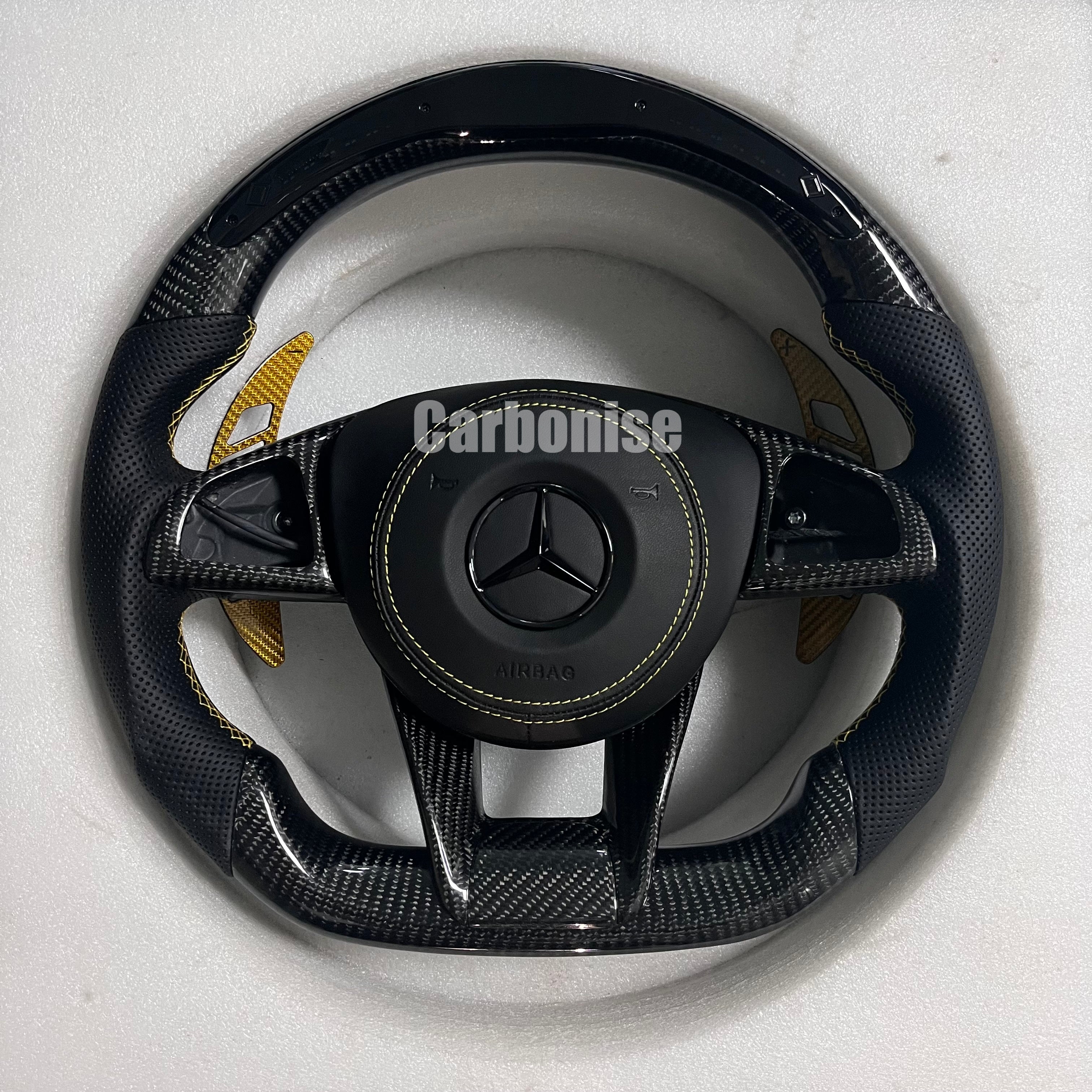 Custom Mercedes-Benz AMG steering wheel featuring gloss carbon fiber, black perforated leather grips with yellow stitching, and vibrant yellow paddle shifters.