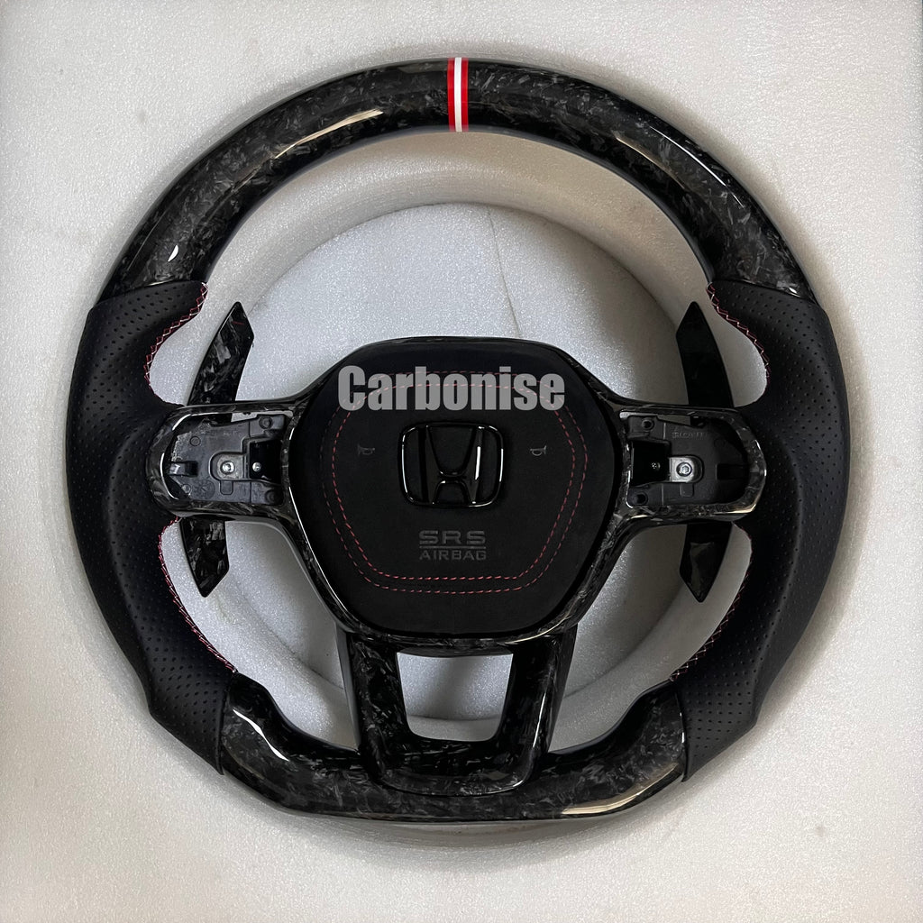 Custom Honda steering wheel with forged carbon top and bottom, black perforated leather side grips, red stitching, and red center stripe.