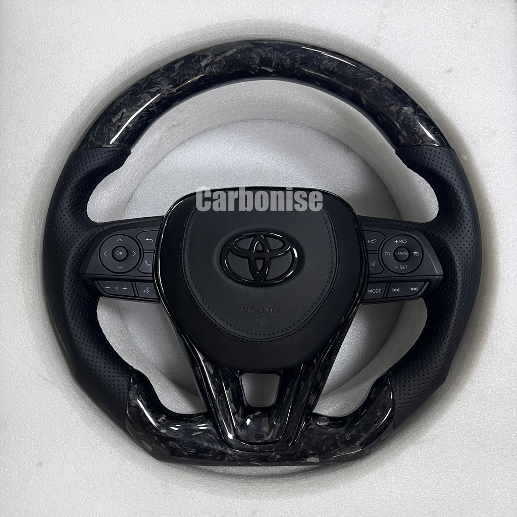 Carbonise carbon fiber Toyota steering wheel with gloss forged carbon top and bottom, perforated leather grips, and OEM multifunction buttons
