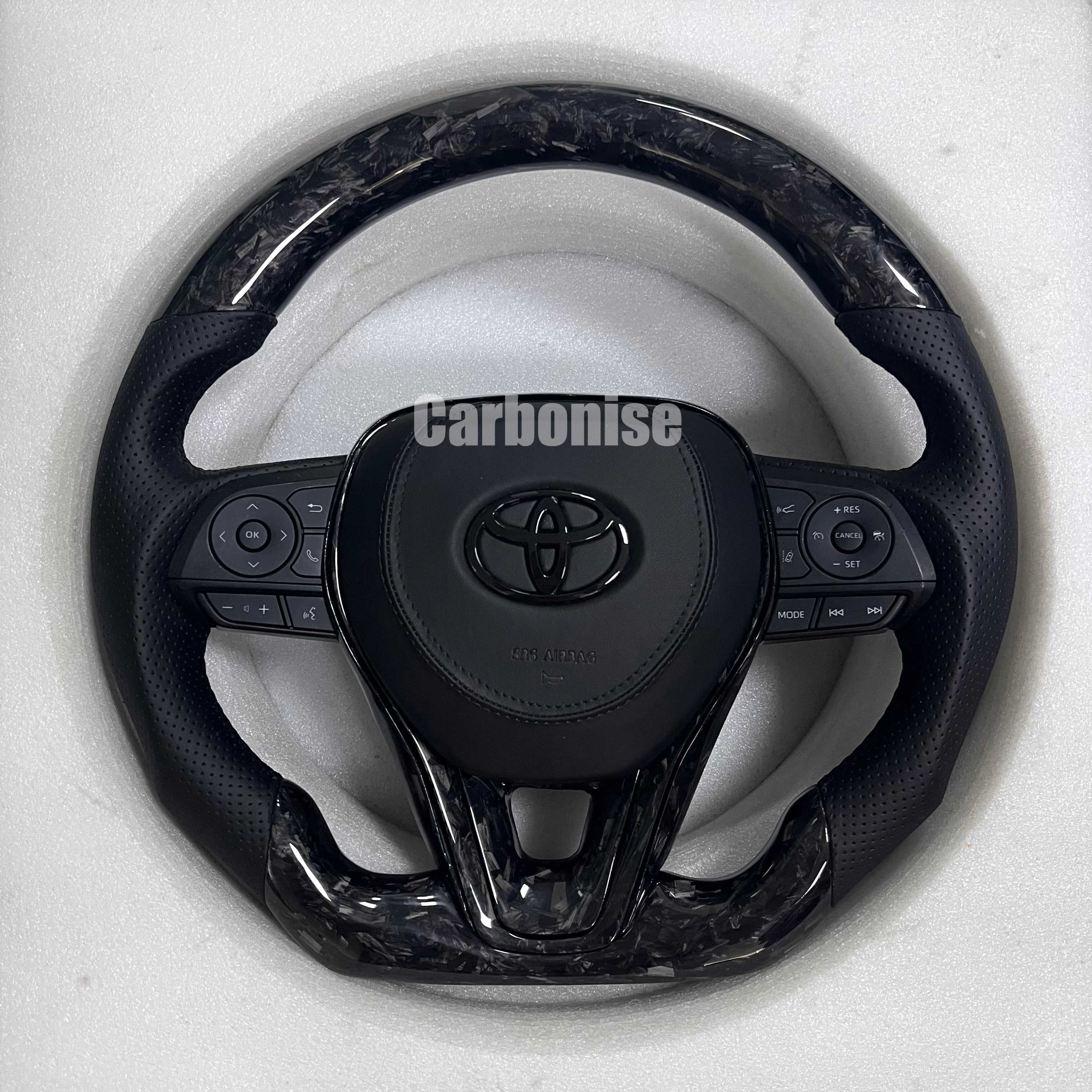 Carbonise carbon fiber Toyota steering wheel with gloss forged carbon top and bottom, perforated leather grips, and OEM multifunction buttons