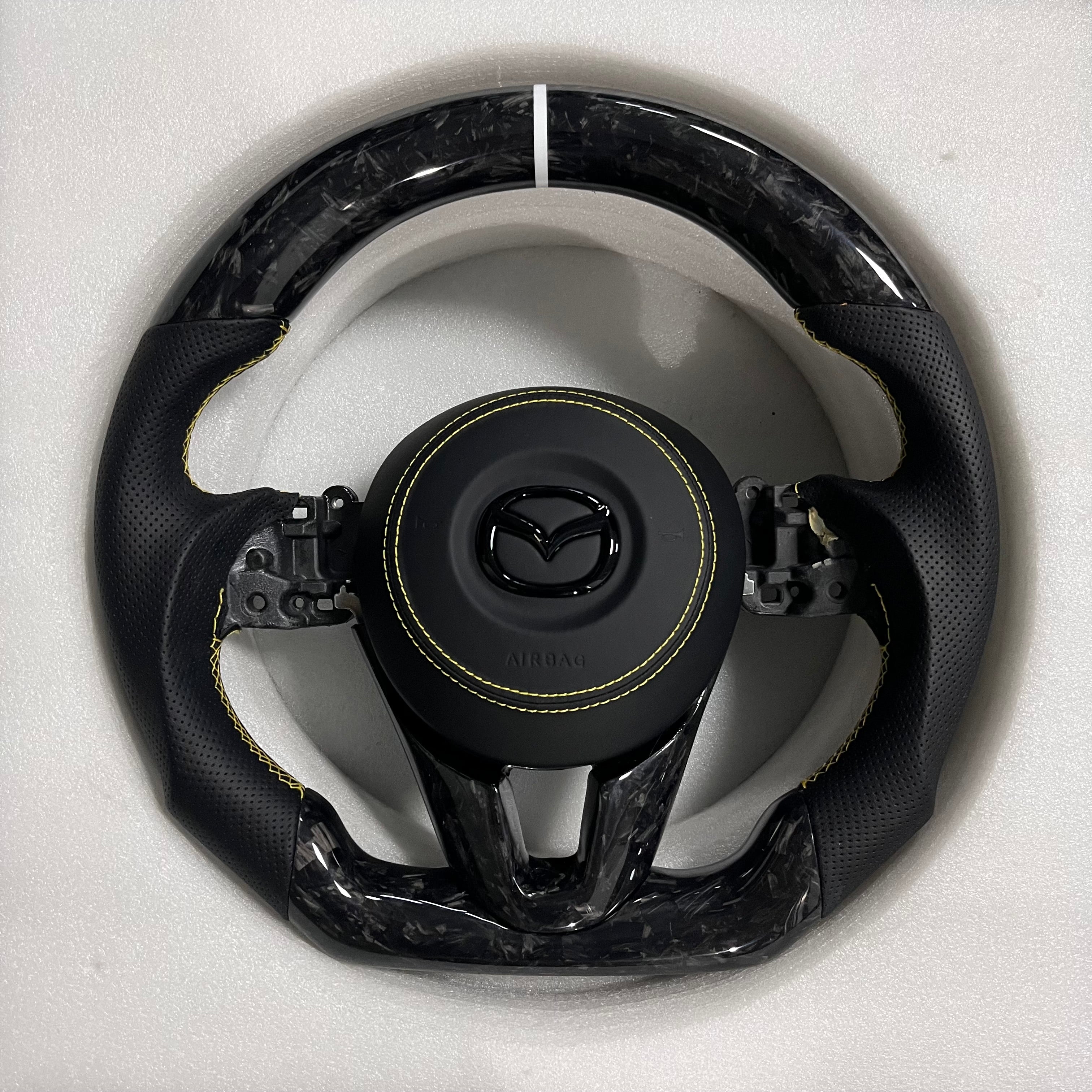 Carbonise Mazda forged carbon steering wheel with black perforated leather grip and yellow stitching