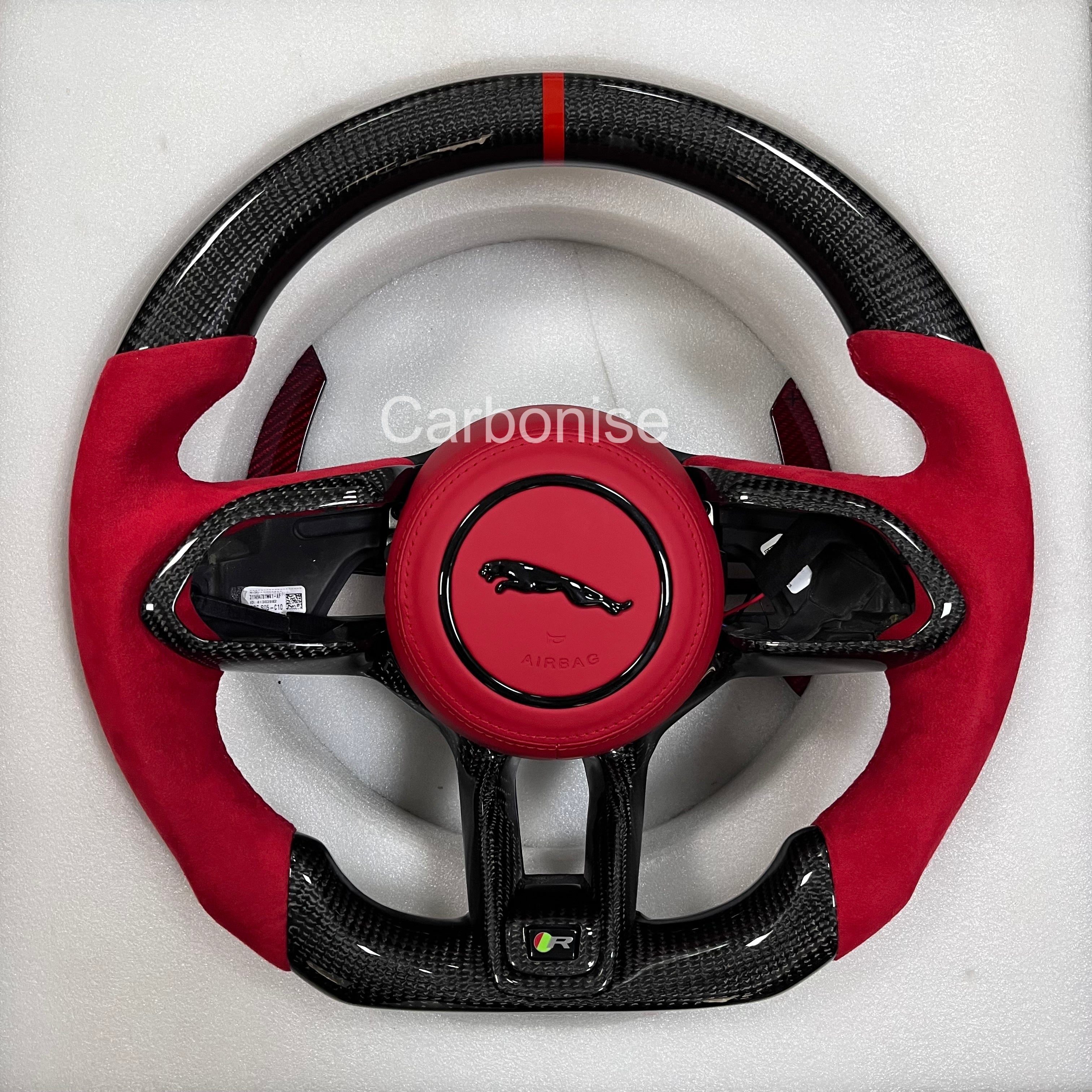 Custom Jaguar R carbon fibre steering wheel with red Alcantara grips, red leather airbag cover, centre alignment stripe, and flat-bottom sport design.