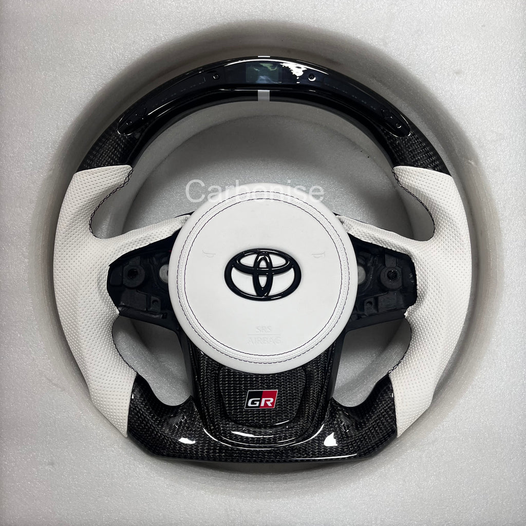 Carbonise Supra carbon fiber steering wheel with white perforated leather grips, white airbag cover, flat bottom design, GR badge, and OEM button layout, led shift light