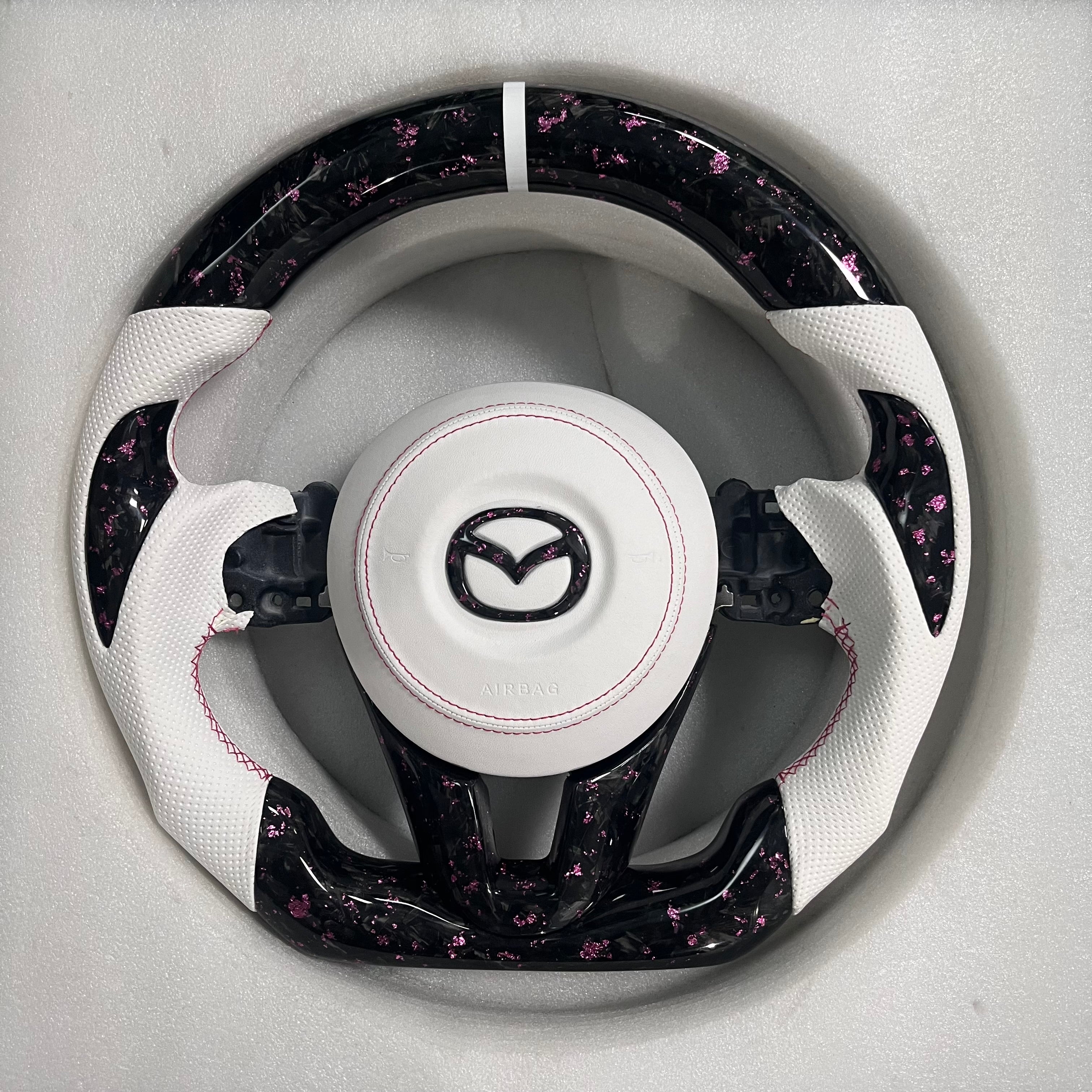 Carbonise Mazda pink forged carbon steering wheel with white perforated leather grip and pink stitching
airbag cover